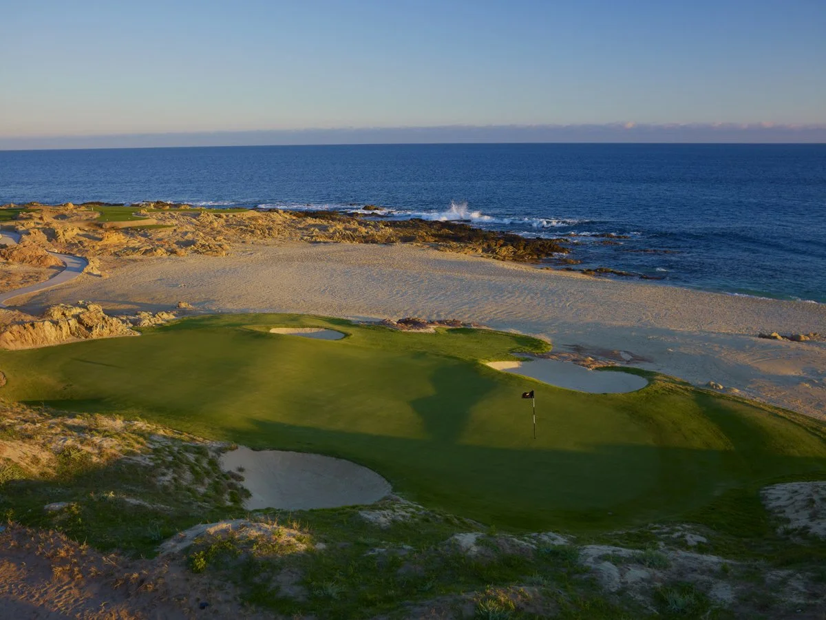 A golf course located on a sandy beach overlooking the ocean at sunset.