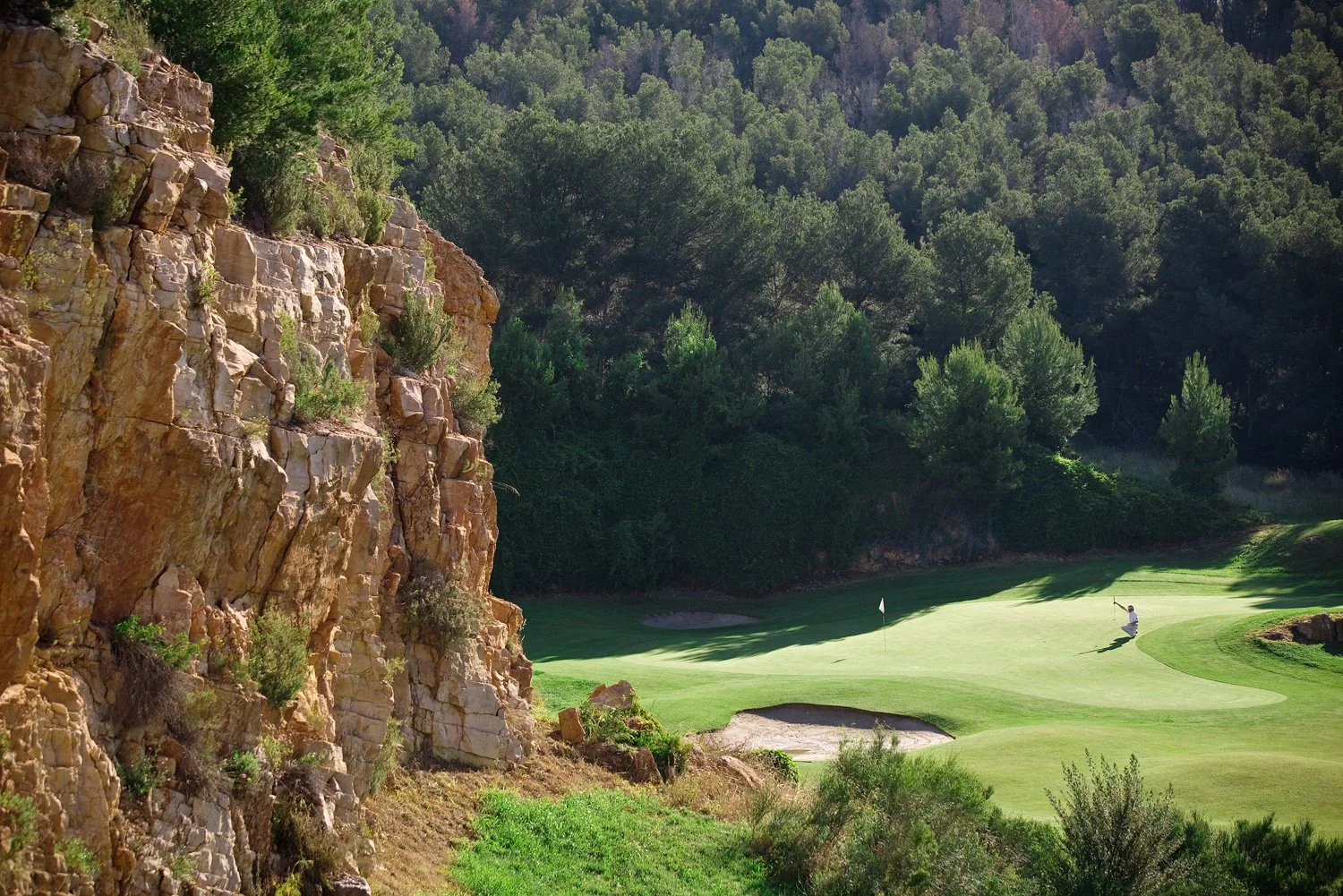 "A golfer preparing to putt on the green of the 3rd hole at Le Fregate Provence Golf Course, which is surrounded by trees."