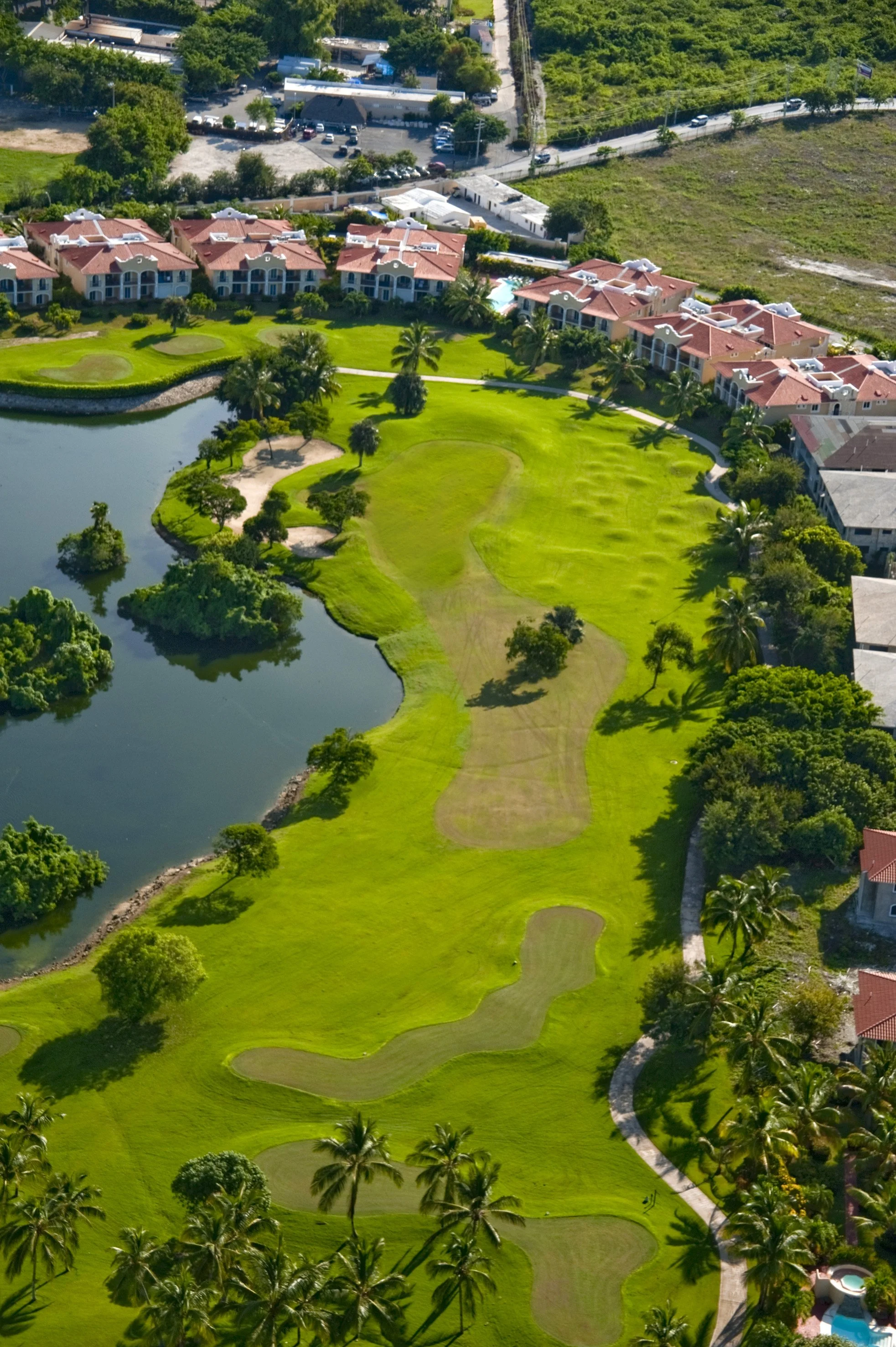 Aerial view of a golf course surrounded by residential buildings, water features, and lush green trees.