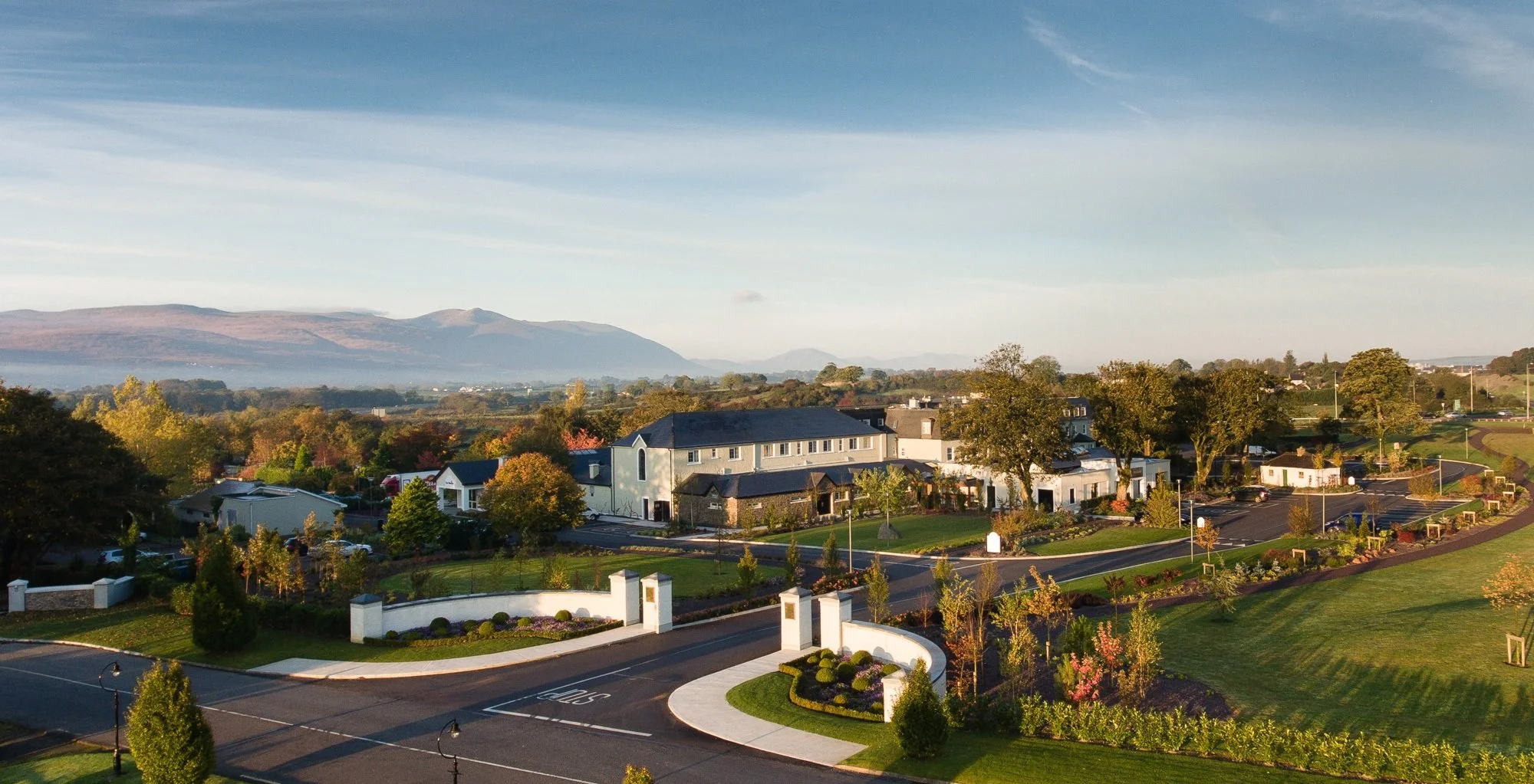 A residential neighborhood with houses, trees, and a winding road, with mountains in the background on a clear day.