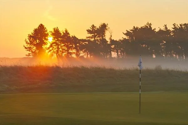Sunrise over a golf course with a flagstick on the green.