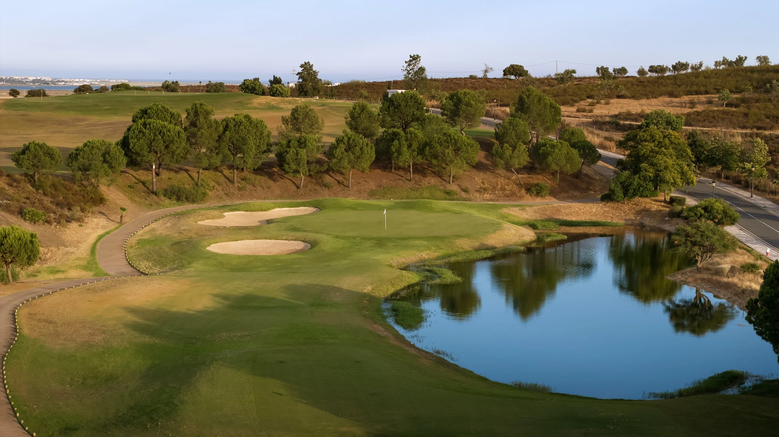 Golf course with green, sand traps, water hazards, surrounded by trees and rolling hills.