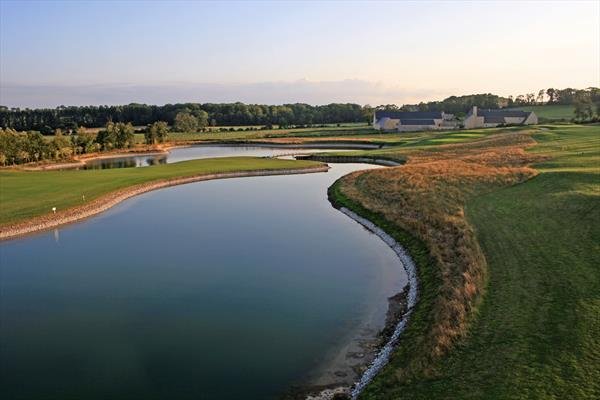 A golf course with water hazards and well-maintained grass, with some trees and buildings in the background during sunset.