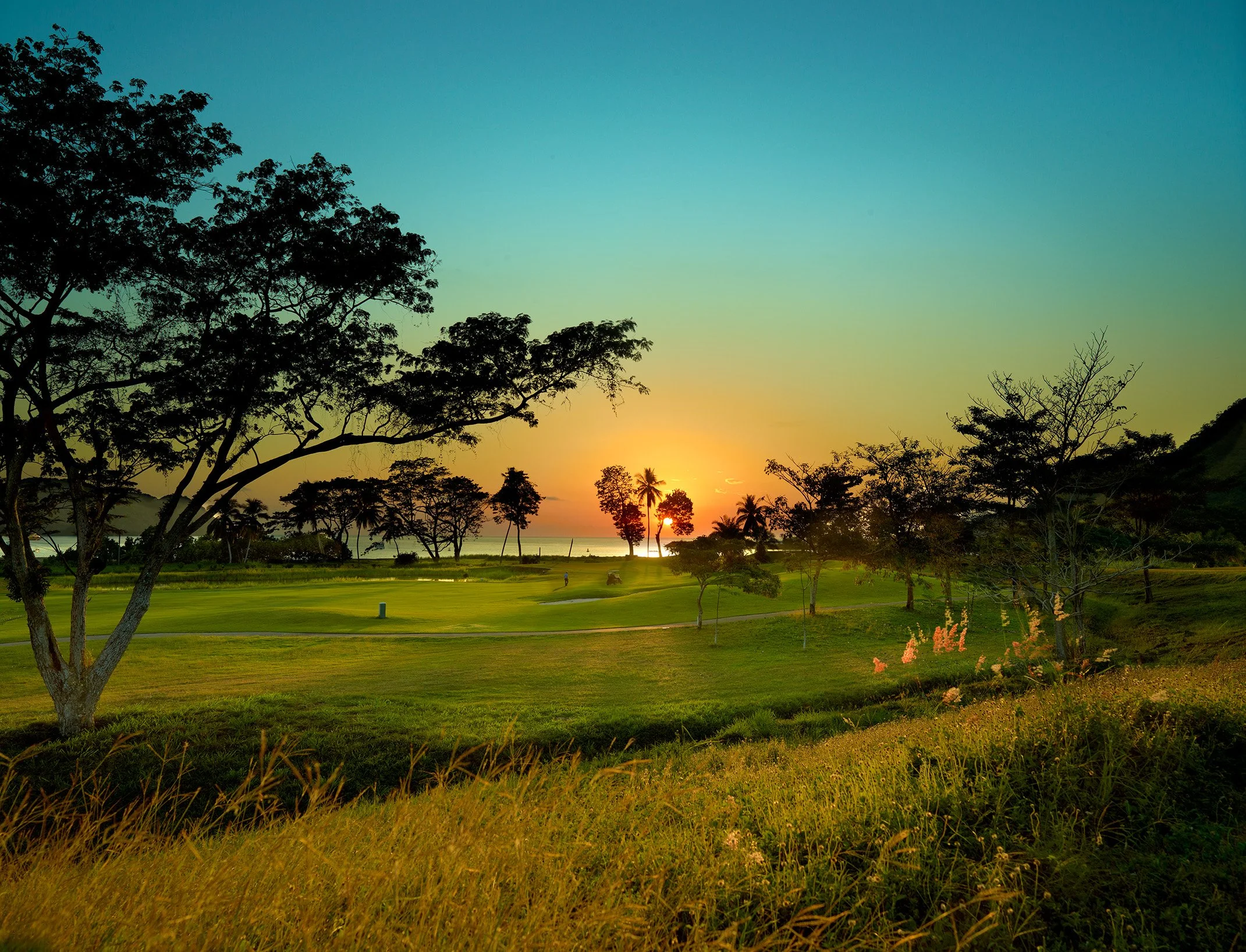 Sunset over a tropical golf course with trees and grassy areas.