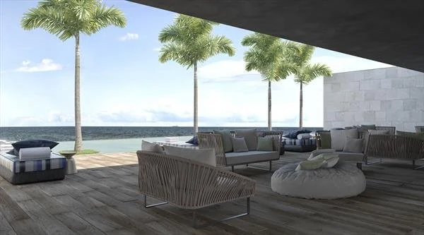 Modern outdoor terrace with palm trees, seating area with sofas, chairs, and a round pouf, overlooking the ocean.