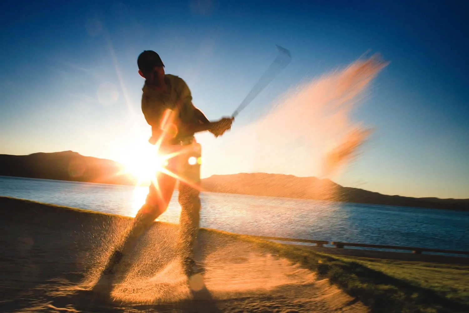 Person water skiing on a lake at sunset with a mountain view in the background.