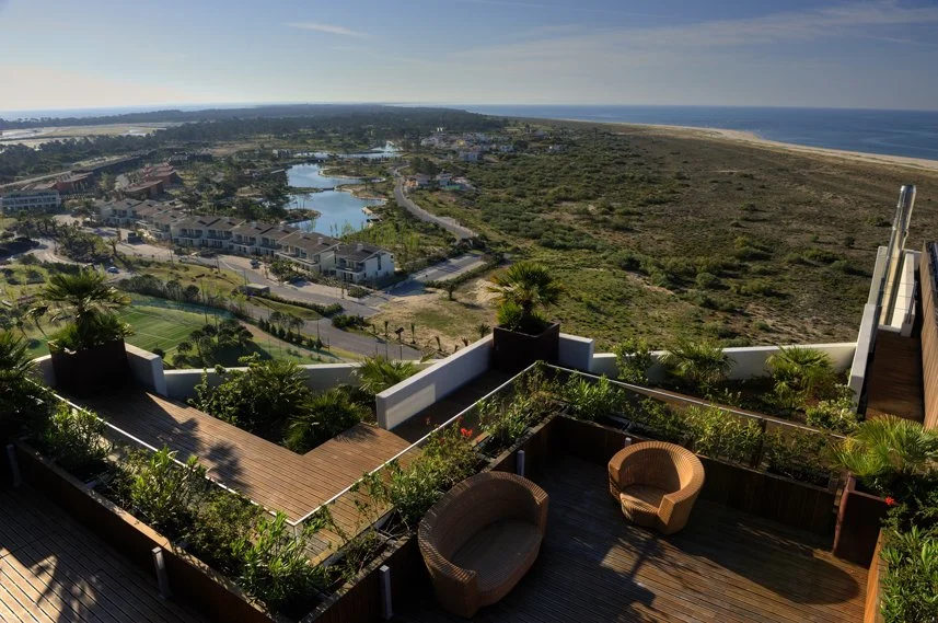 Aerial view of a coastal resort area with buildings, lakes, a river, open land, and the ocean in the distance.