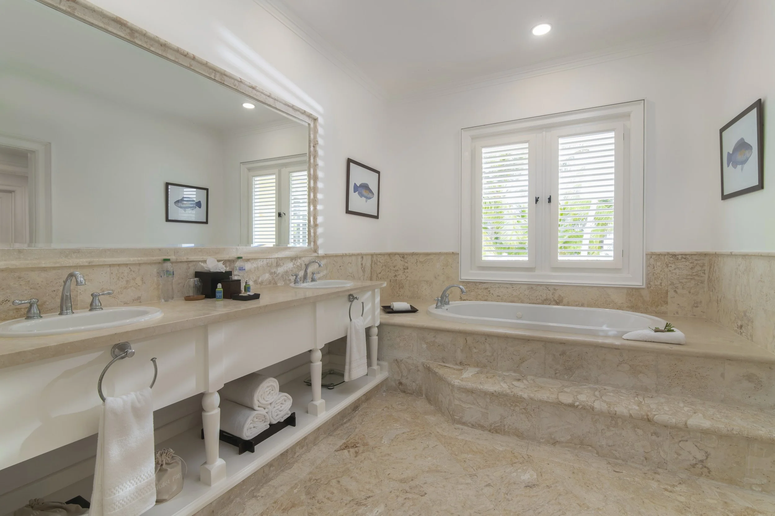 Bathroom with double sink vanity, large mirror, bathtub under window, and framed fish artwork