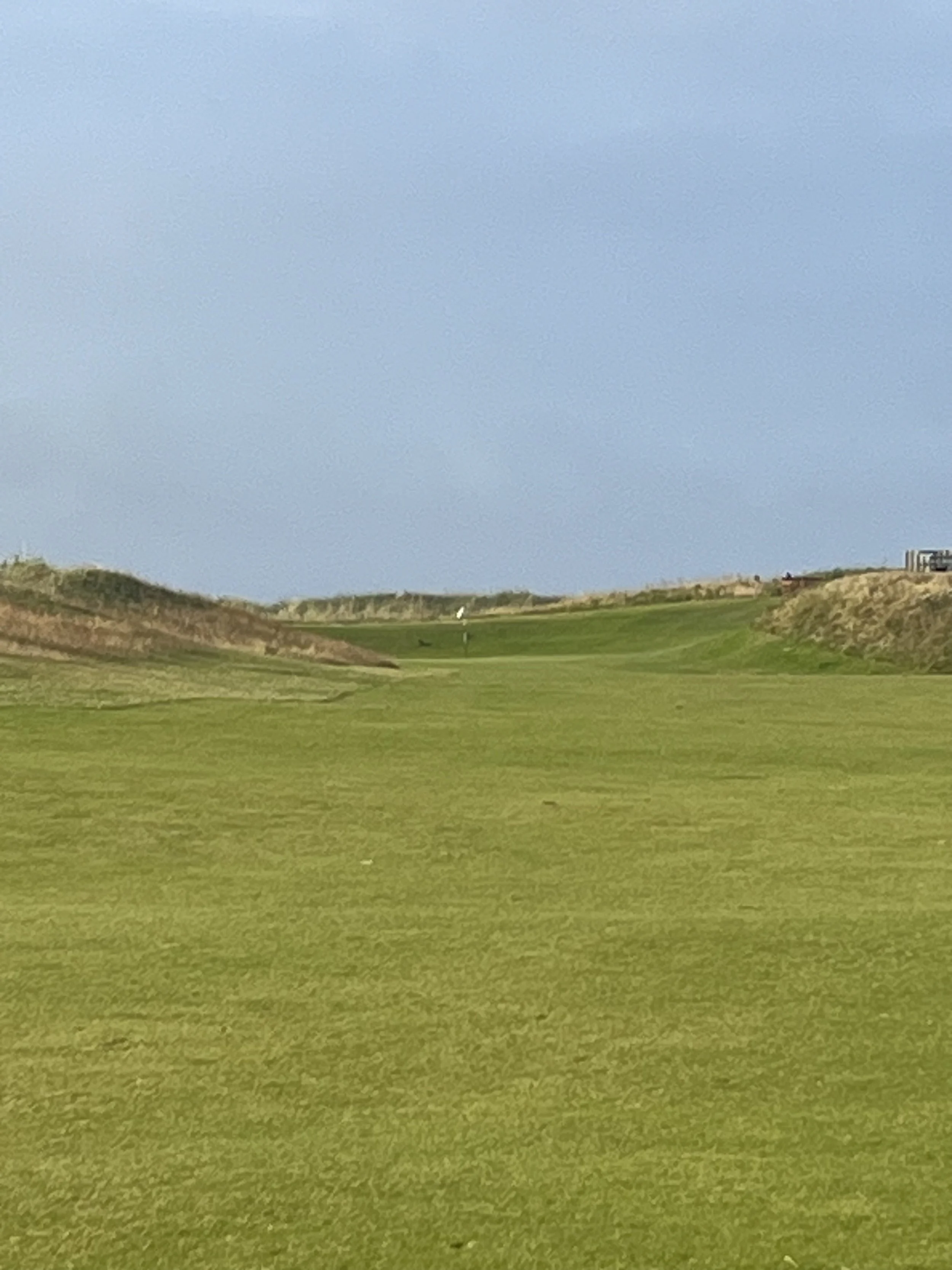 Green golf course fairway with sand dunes and a cloudy sky.