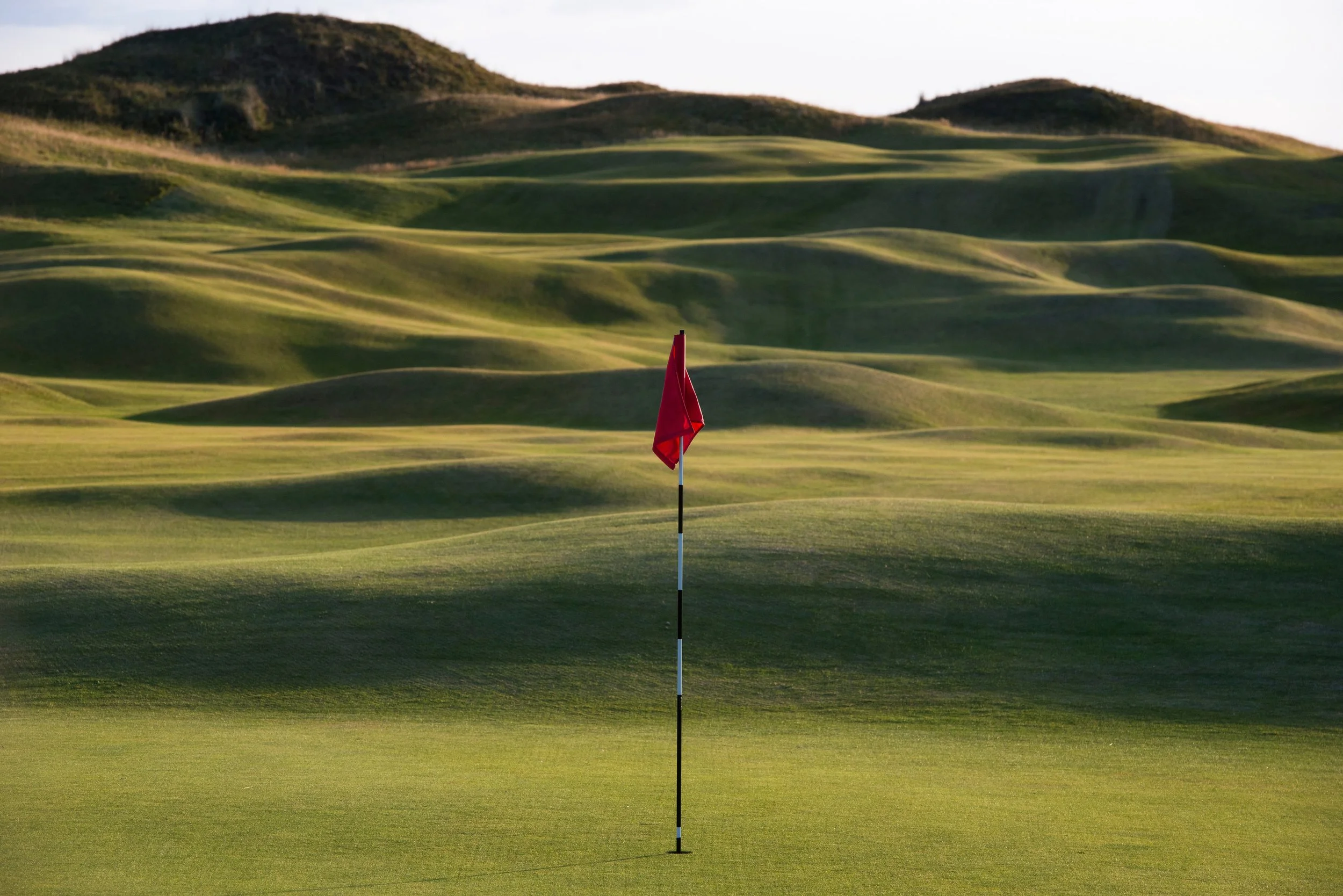 A red flag on a golf green with rolling hills in the background.