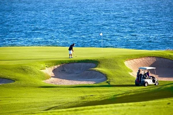 A person preparing to putt on a golf course near a body of water, with a golf cart nearby.