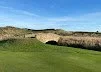 A golf course with a green field, sand traps, and a scenic backdrop of hills under a clear blue sky.
