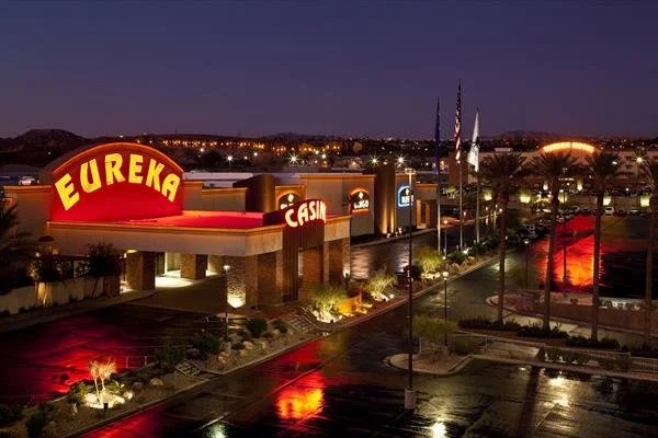 Night view of Eureka Casino with illuminated neon signs, palm trees, and reflective wet pavement.