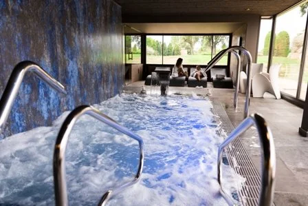 Indoor hot tub with seating area and large windows showing outdoor greenery.