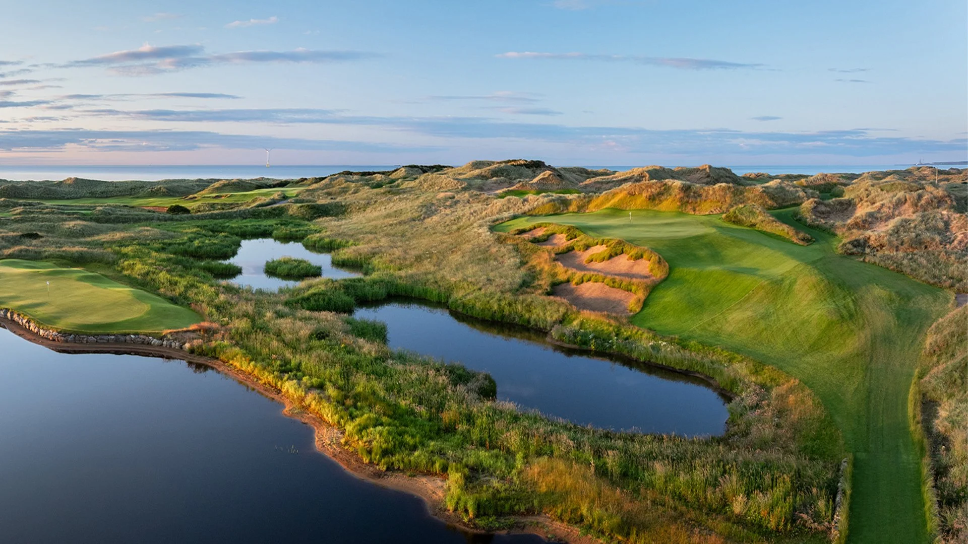 A stunning elevated view of the green fairways, deep bunkers, and serene water hazards nestled among large sand dunes at Trump International Golf Links Aberdeenshire, a spectacular destination on our luxury escorted golf tours in Scotland.
