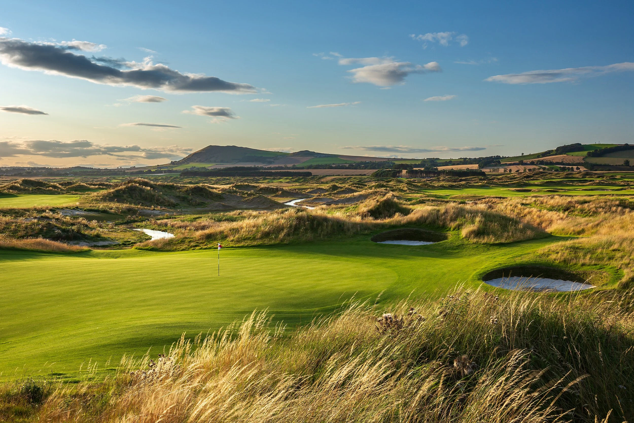 A panoramic view of the rolling green fairways, tall fescue grass, and deep pot bunkers at Dumbarnie Links, a spectacular modern coastal course featured on our luxury escorted golf tours to Scotland.