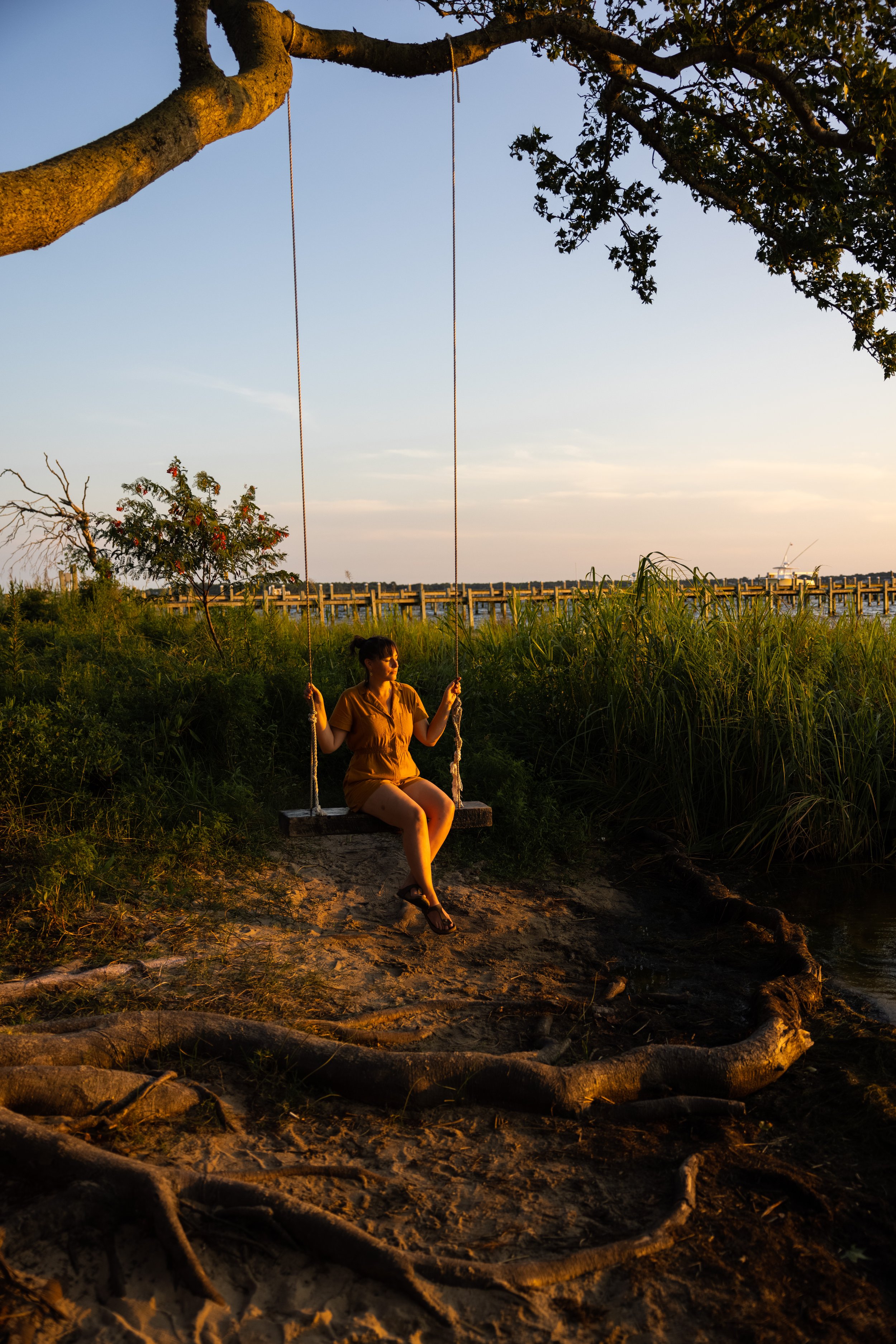 a woman in a yellow jumper sits on a tree swing