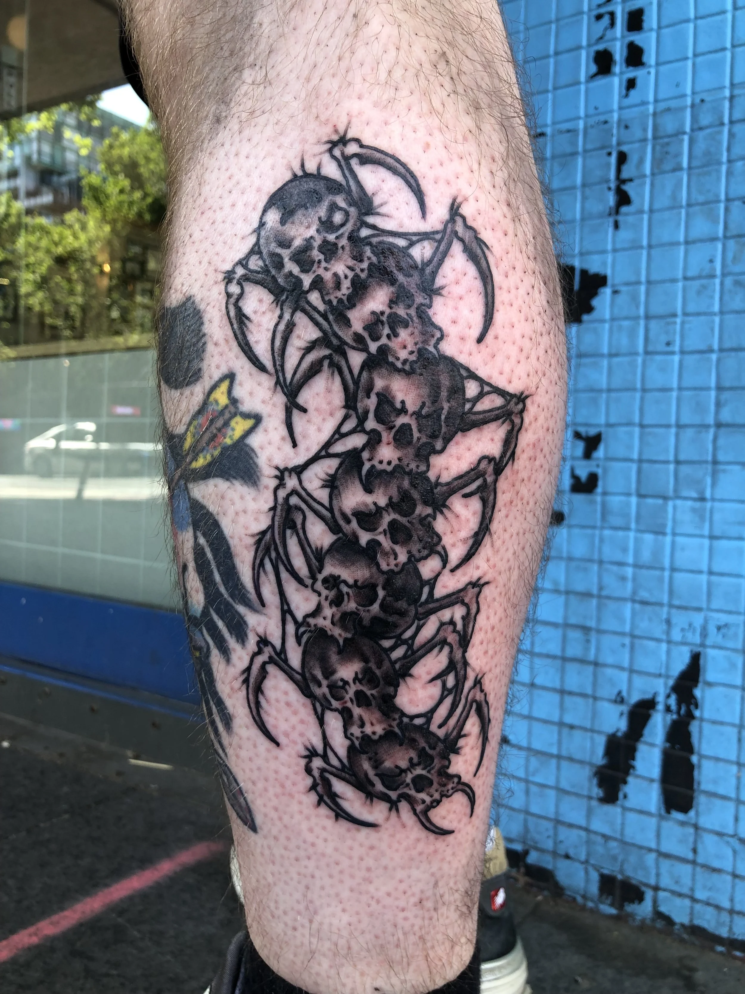 Tattoo of four black and gray skulls with spider-like legs on a person's leg, made at Thanks Tattoo