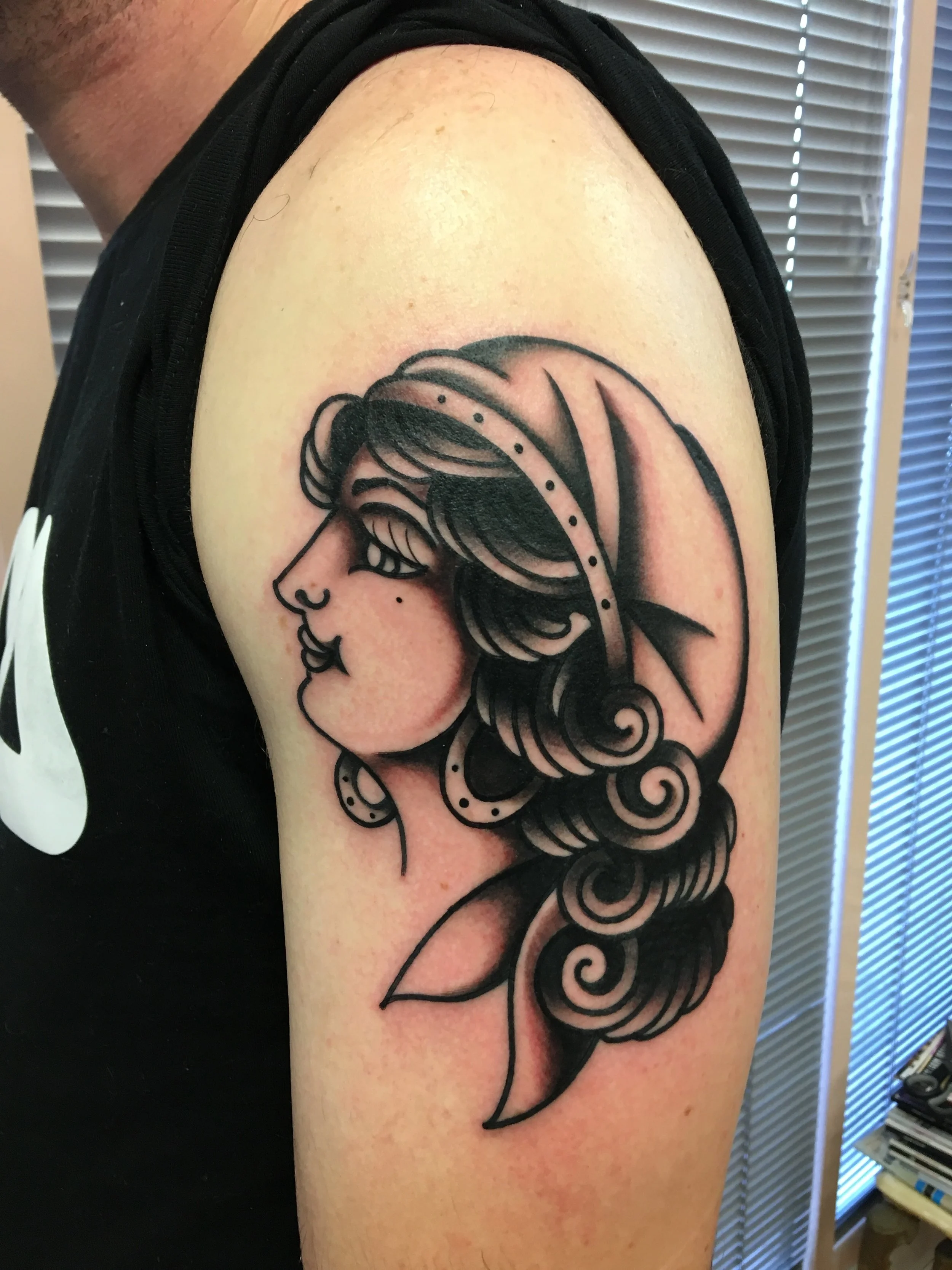 Tattoo of a woman's face and hair with decorative swirls on upper arm, made at Thanks Tattoo