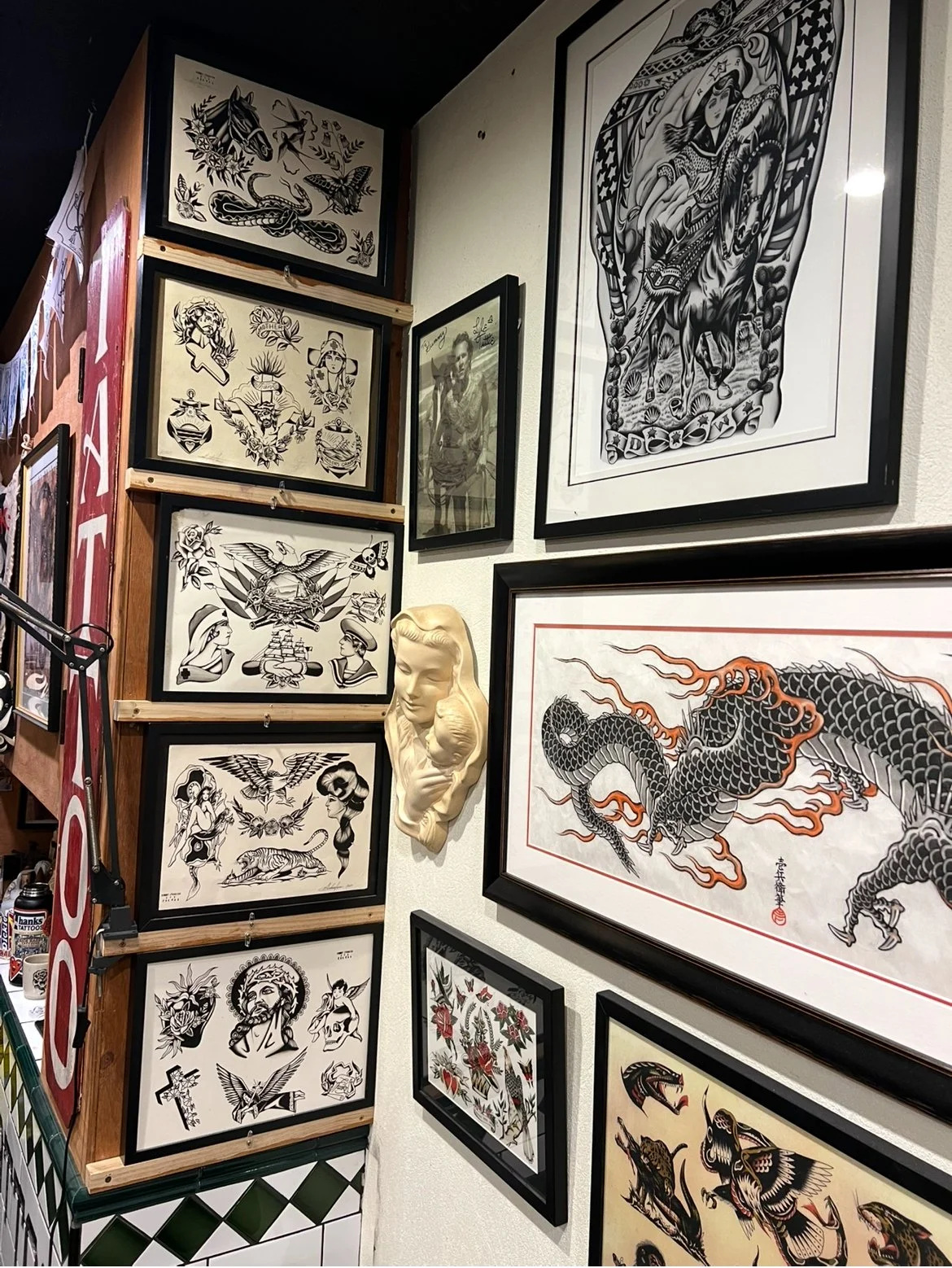 Wall decorated with various tattoo artworks, including a dragon, a woman with a sword, and traditional American tattoo style designs, inside Thanks Tattoo shop