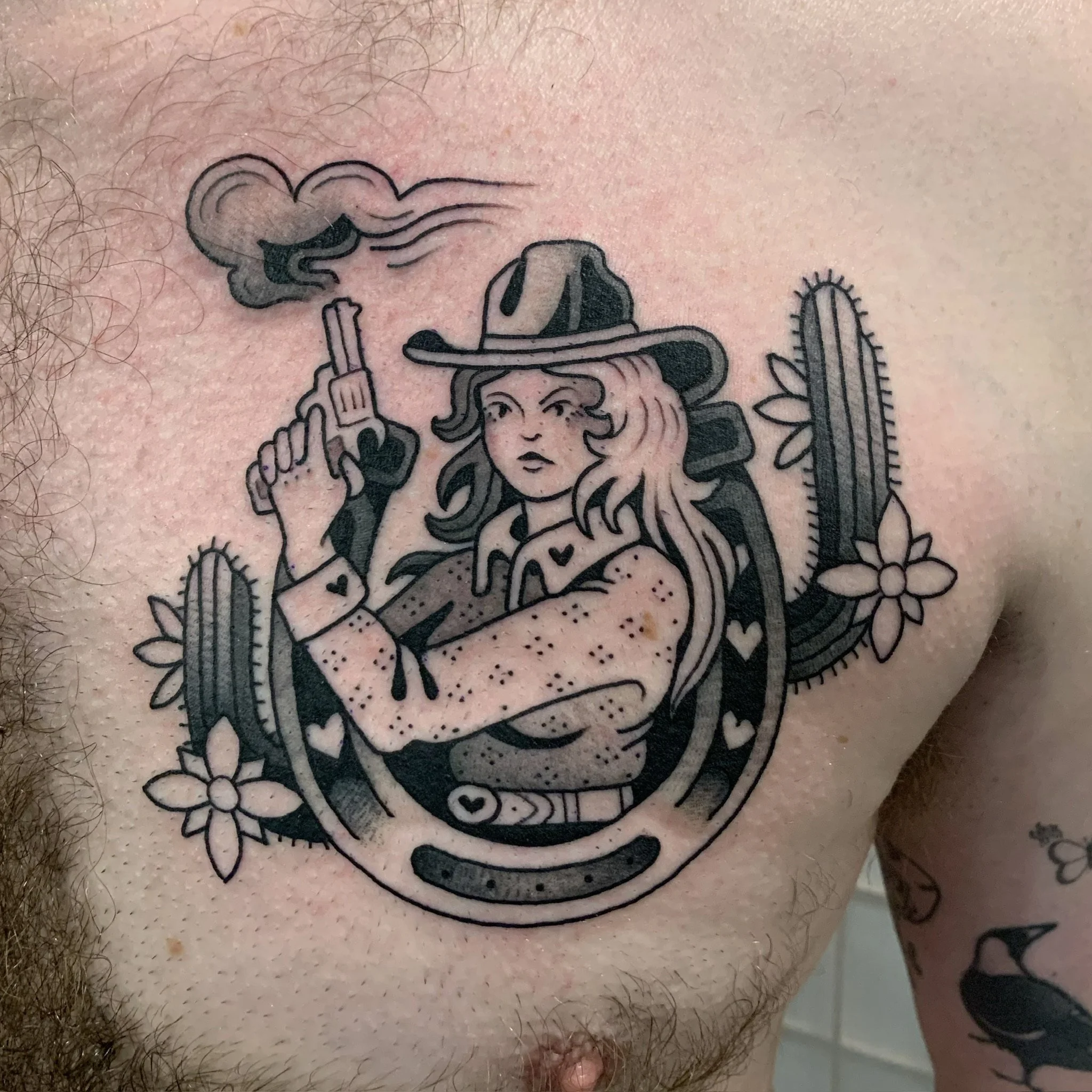Tattoo of a woman with long hair wearing a cowboy hat, holding a gun with smoke, surrounded by cactus plants and flowers, made at Thanks Tattoo