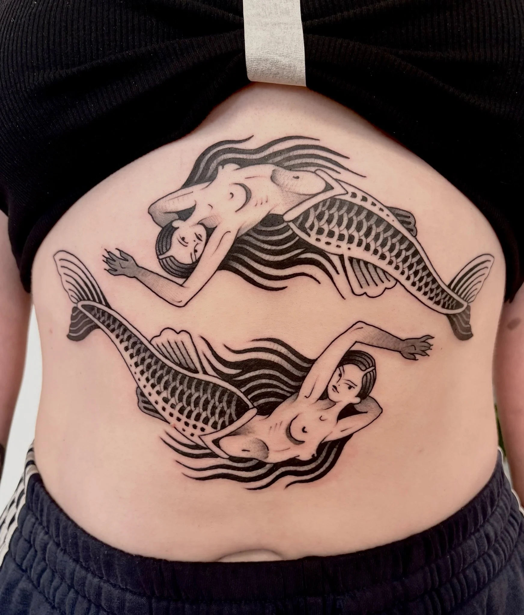 Tattoo of two mermaids with long flowing hair, intertwined and facing each other, on a person's side ribcage, made at Thanks Tattoo