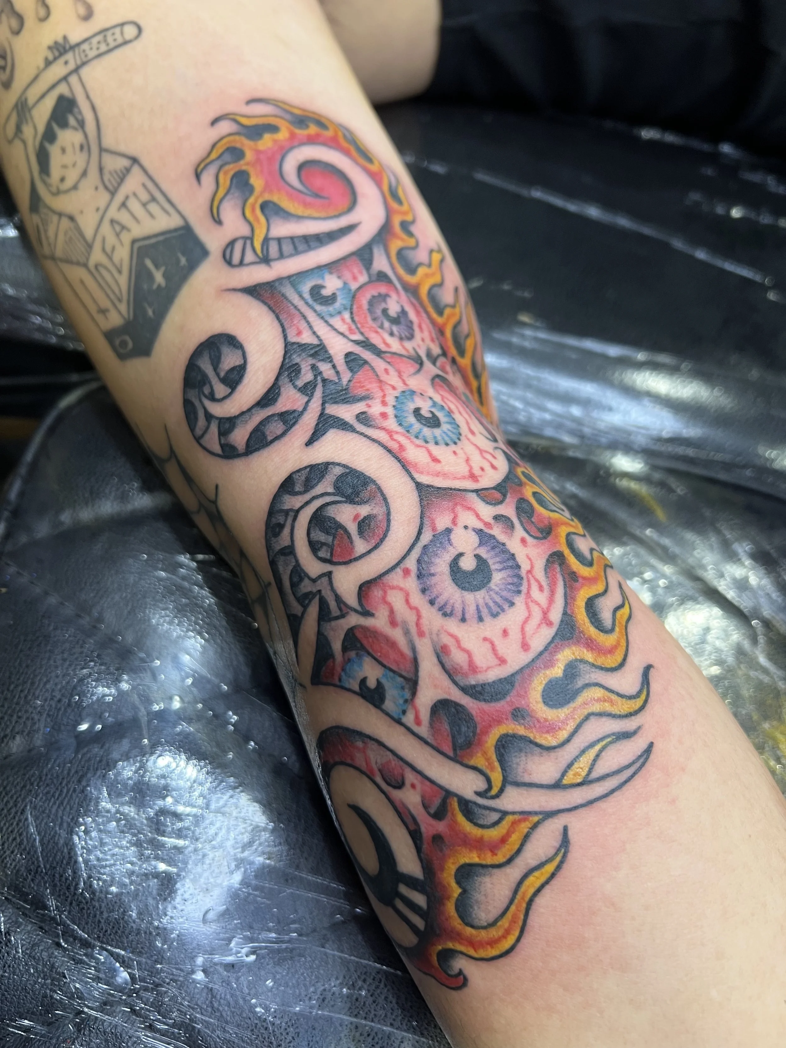 A tattoo of three eyes with flames surrounding them on a person's arm, made at Thanks Tattoo