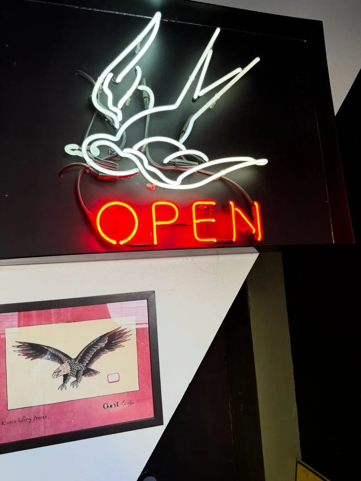 Neon sign of a flying eagle with the word "OPEN" in red neon lights in Thanks Tattoo shop