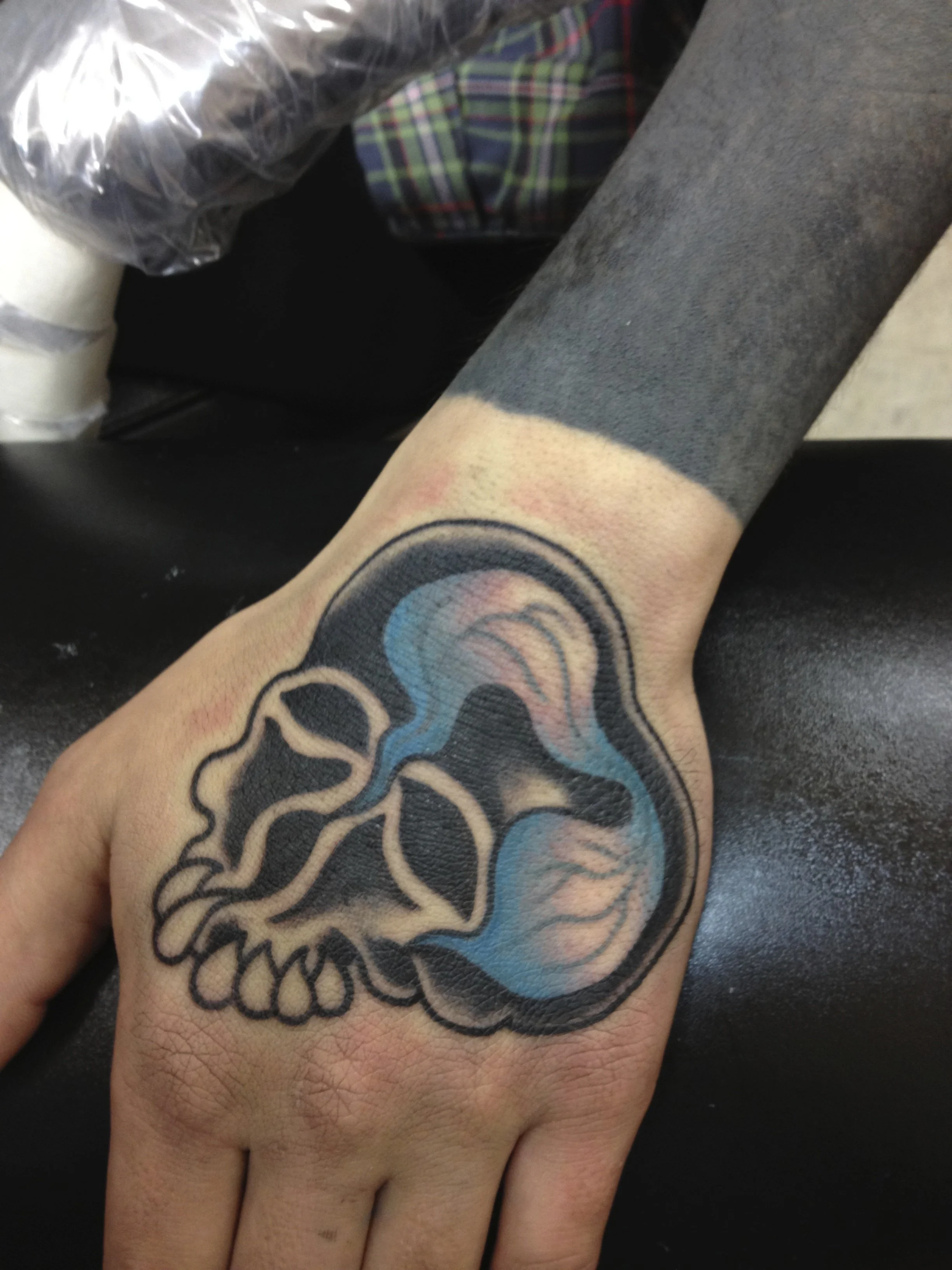 Tattoo of a human skull with stylized lightning bolts inside, on the back of a person's hand, made at Thanks Tattoo