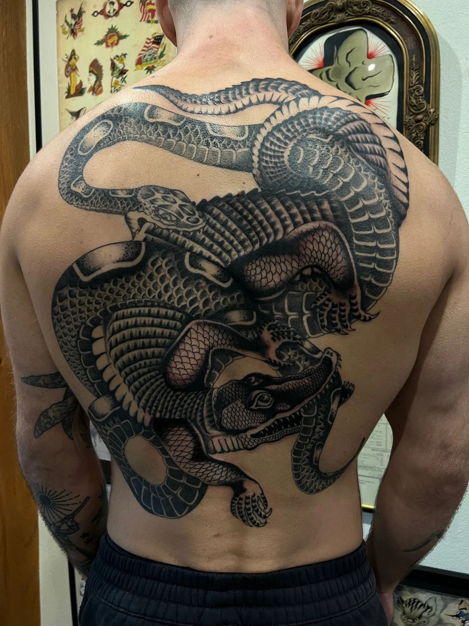 A person's back with a large black and gray tattoo of a snake intertwined with a dragon detail covering the upper and middle back, made at Thanks Tattoo