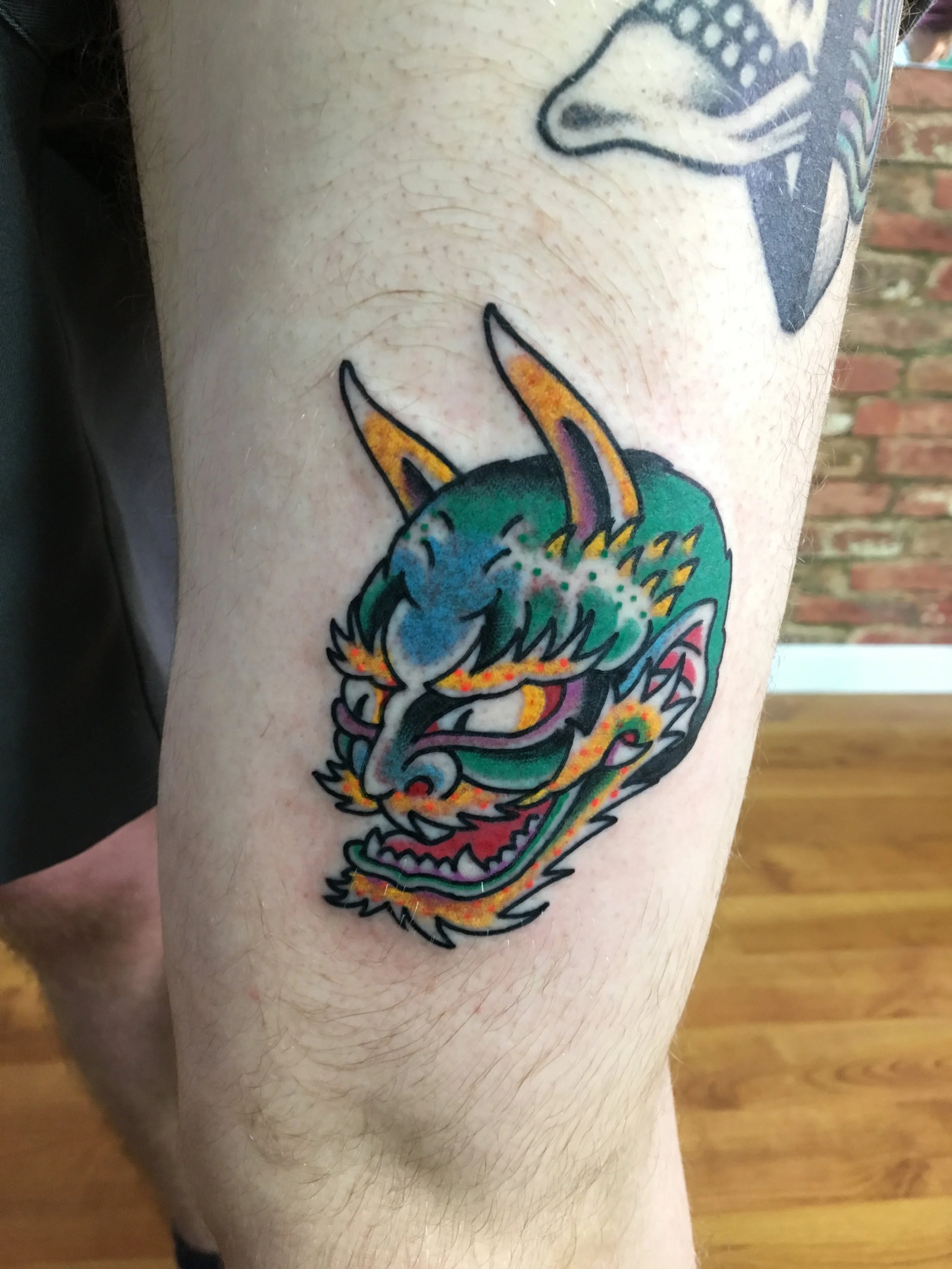 Colourful tattoo of a fierce dragon's head on person's thigh, with vibrant shades of green, blue, orange, and pink, made at Thanks Tattoo
