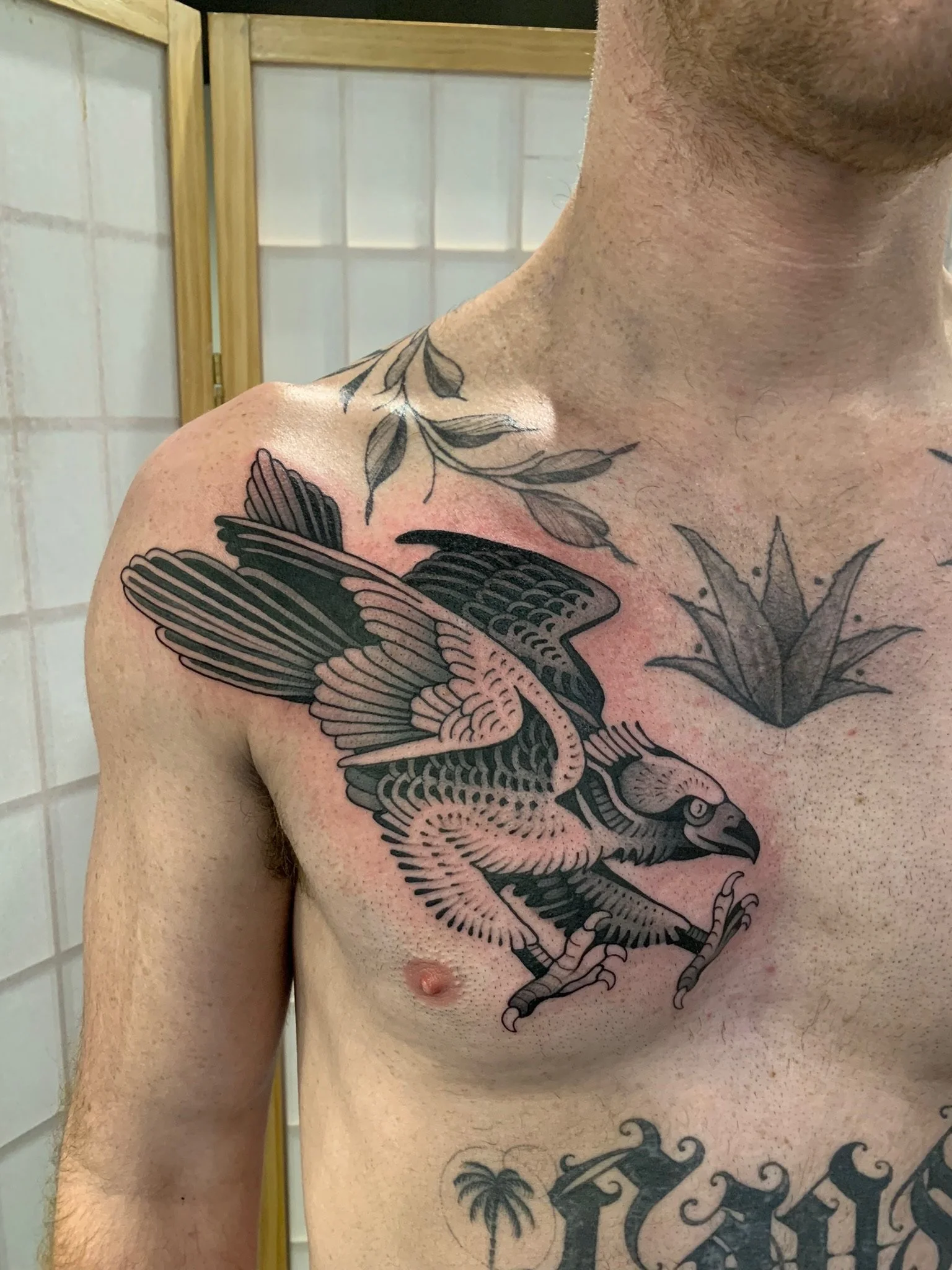 The bird is depicted in black and gray shading with detailed feathers, and its wings are spread with talons extended. Additional floral tattoos are visible on the shoulder and chest, made at Thanks Tattoo