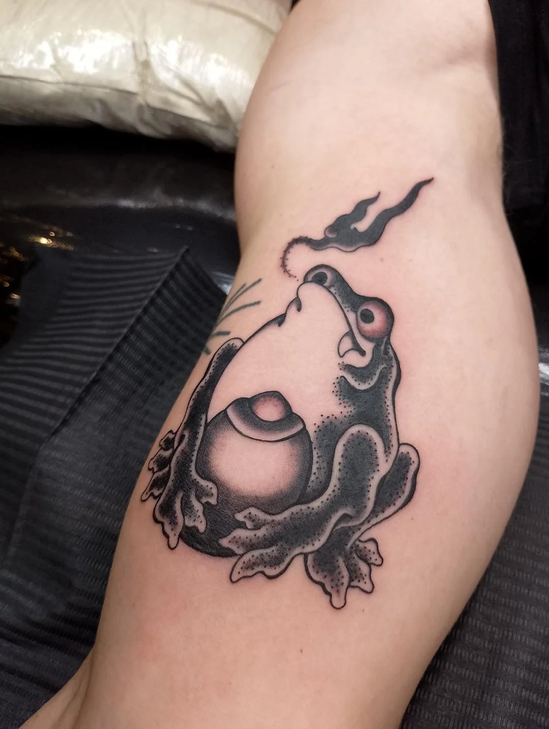 Black and gray tattoo of a frog with smoke coming out of its nostrils on person's upper thigh, made at Thanks Tattoo