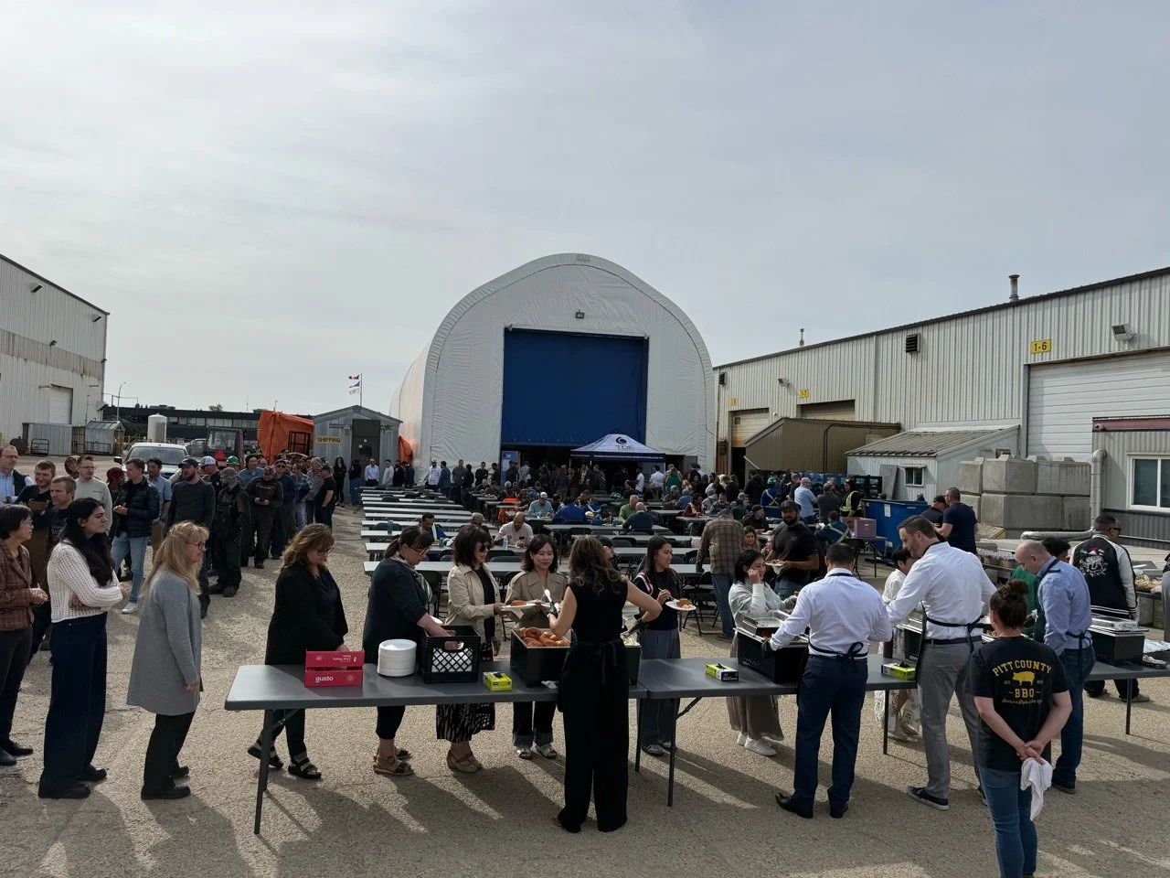 Pitt County BBQ staff and TDE executives serving guests at an outdoor corporate BBQ buffet.