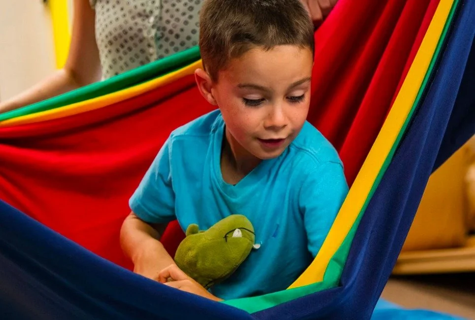 Boy playing in a colorful sensory hammock swing during pediatric occupational therapy