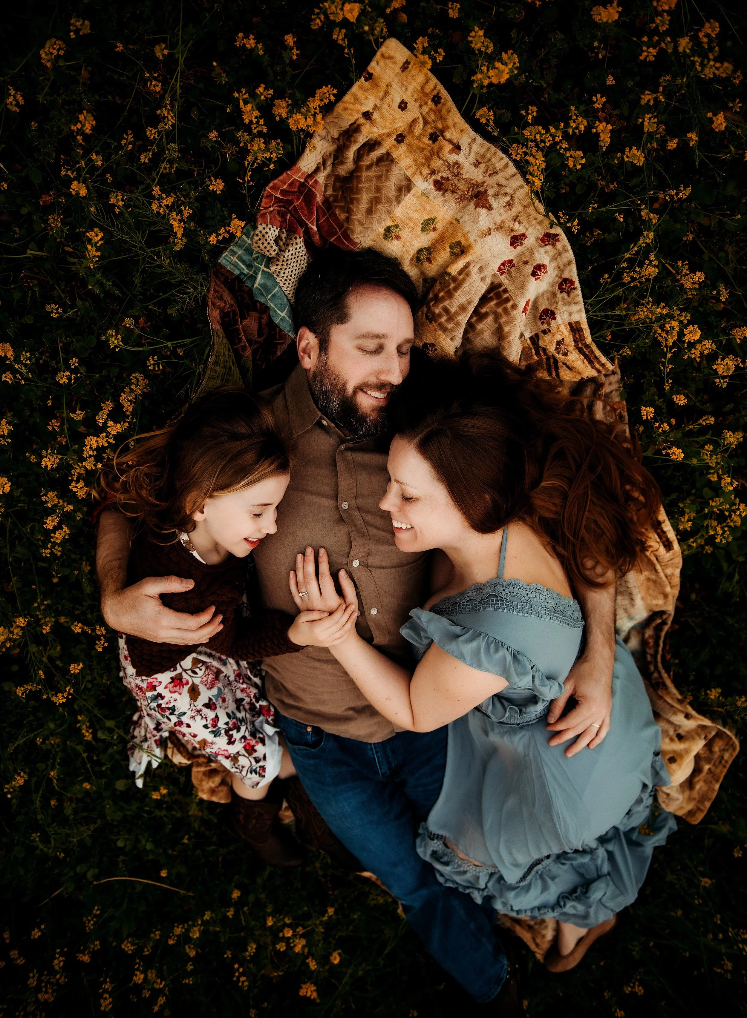 family of 3 laying in the grass at sunset