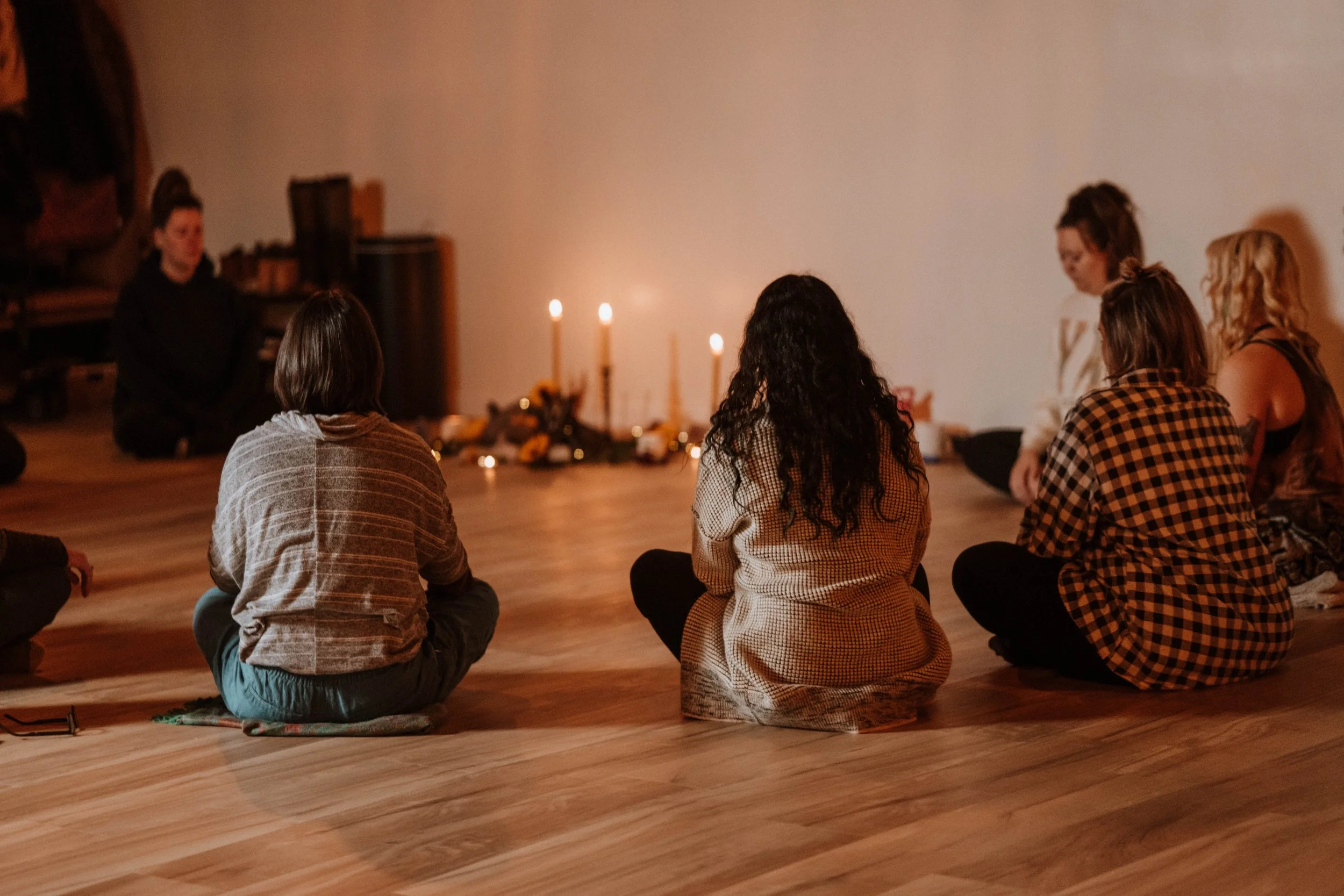 Group of people sitting on the floor in a circle during a meditation or spiritual session, illuminated by candles.