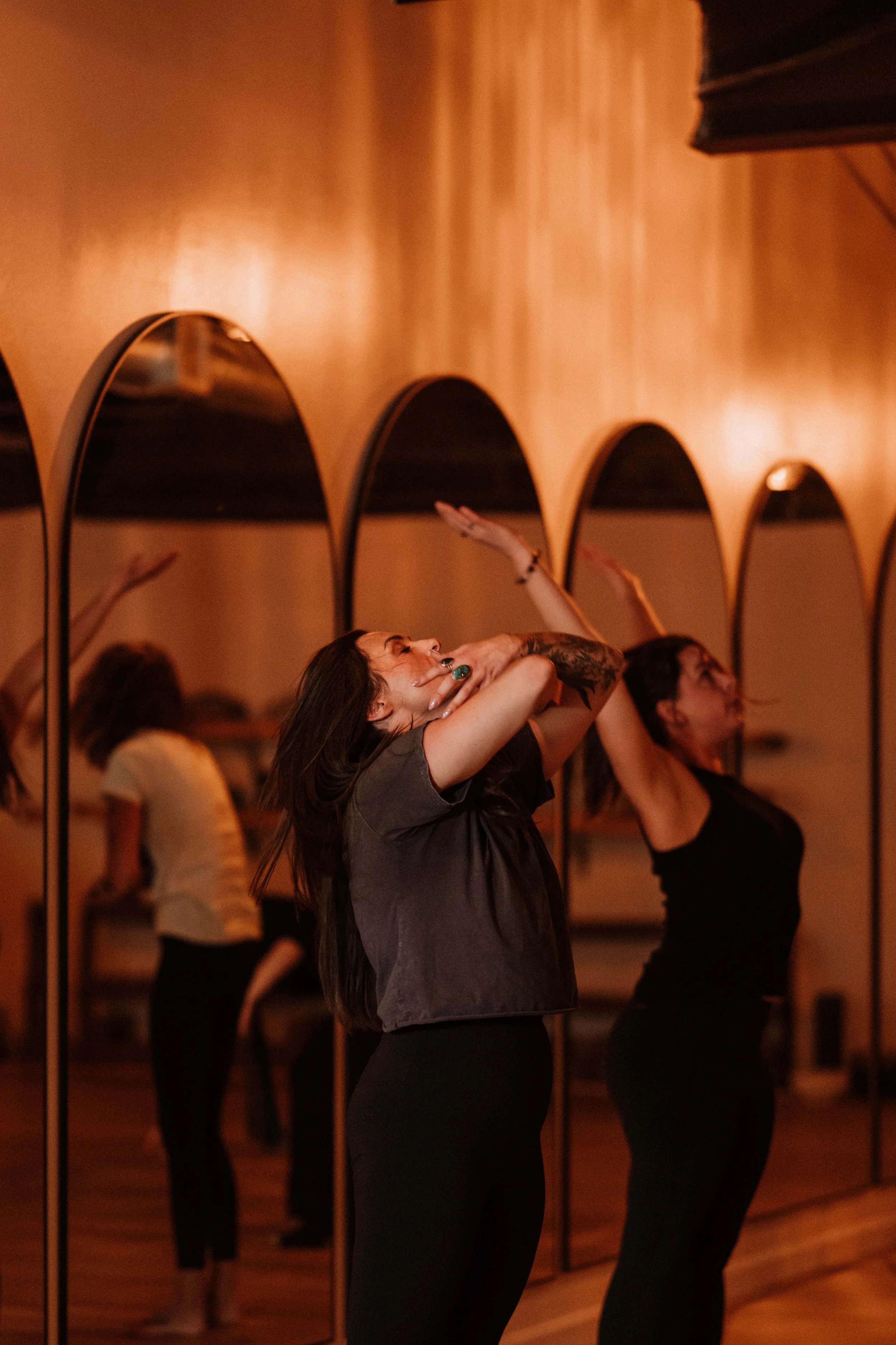 A woman dancing in a studio with a row of mirrors on the wall, capturing her movement and expression.