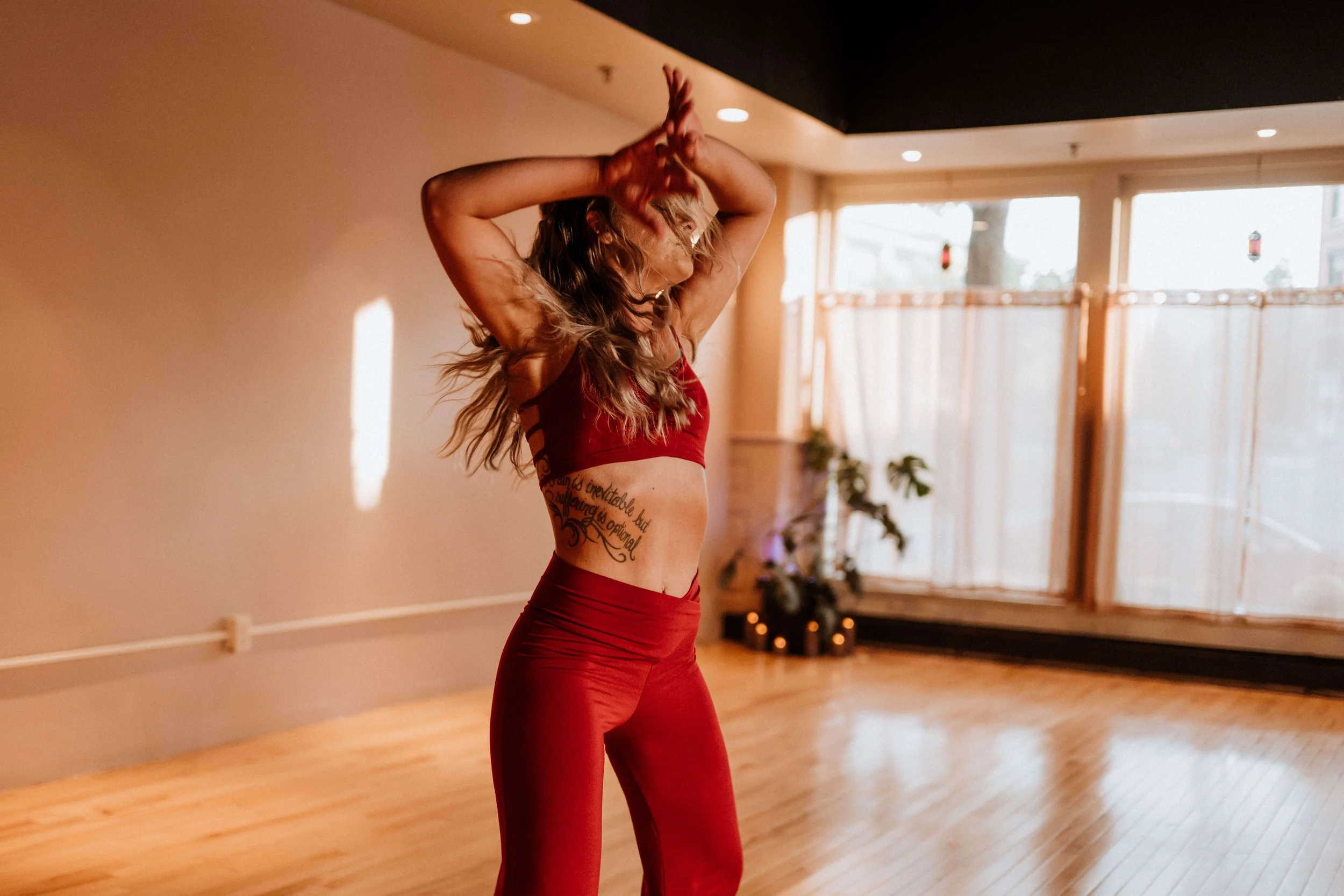 A woman with long hair wearing a red sports bra and matching red leggings dancing in a studio.