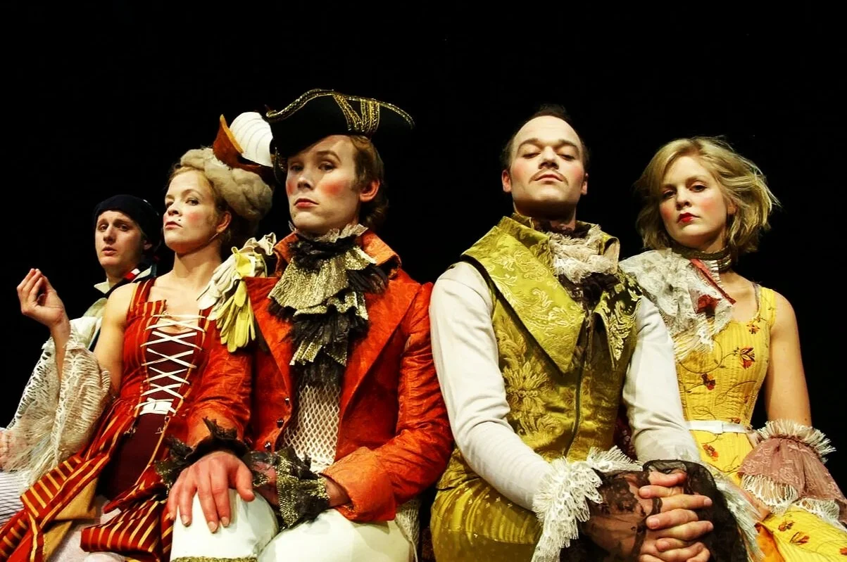 Fem mennesker kledd i barokke kostymer på en teaterscene.