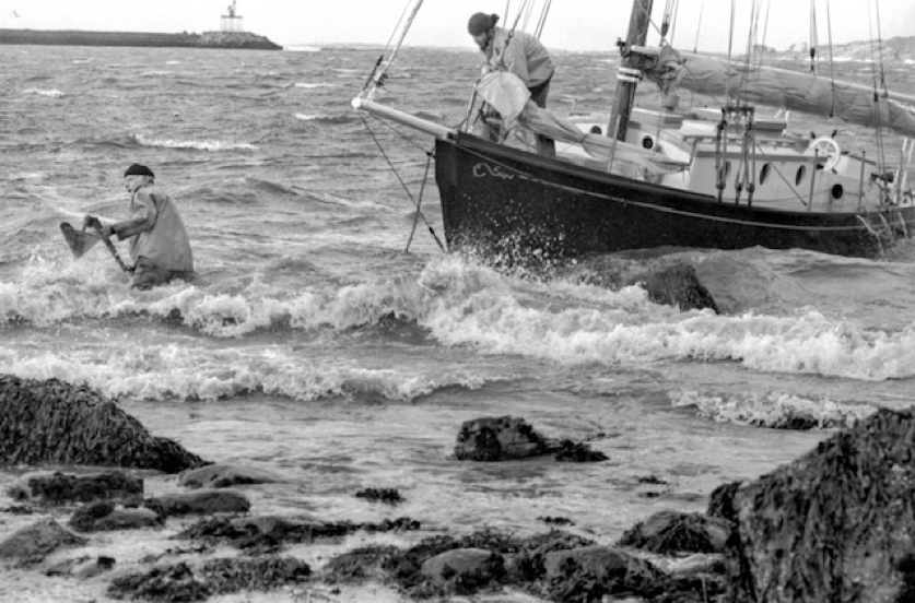   [4] Joe Garland, in the water, and boatwright Larry Dahlmer try unsuccessfully to save Garland's Cruising Club which was wrecked on the Eastern Point rocks in 1980. The Cruising Club was the last boat owned by Gloucester's most famous solo sailor, 