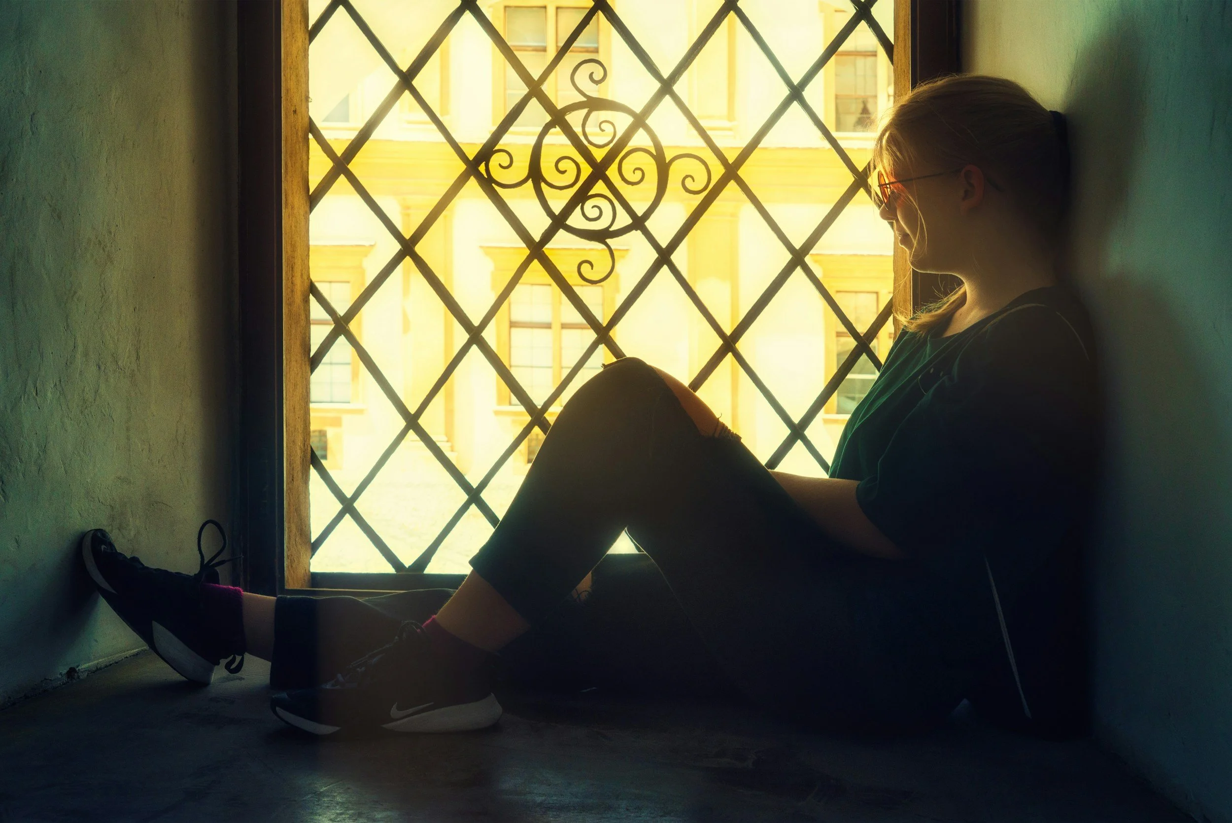 Image of a ginger haired woman sat on a windowsill, looking out through the diamond-leaded window.