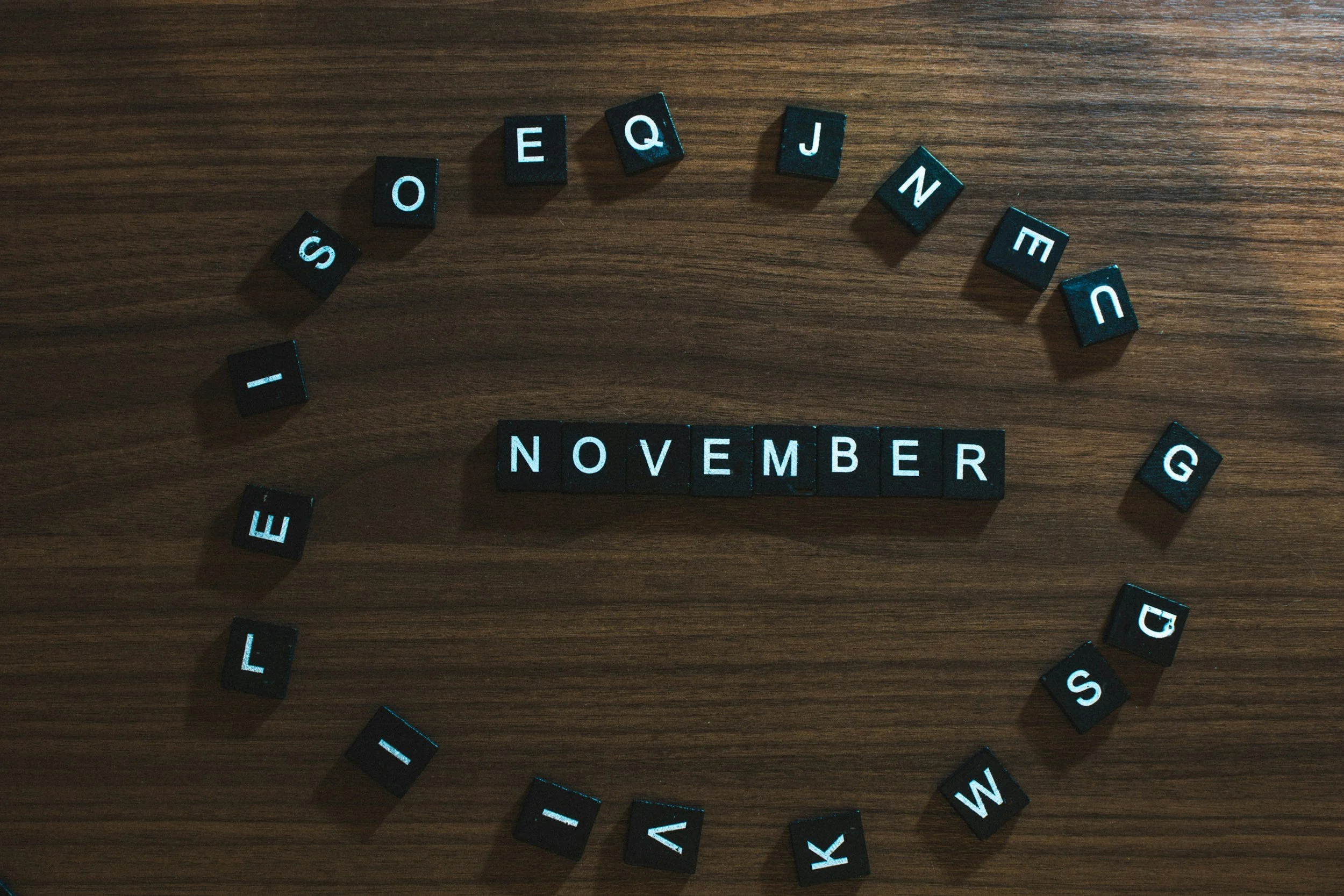 The word 'November' is spelt out in white capital letters on black cubes. Cubes with the other letters of the alphabet encircle 'November.'