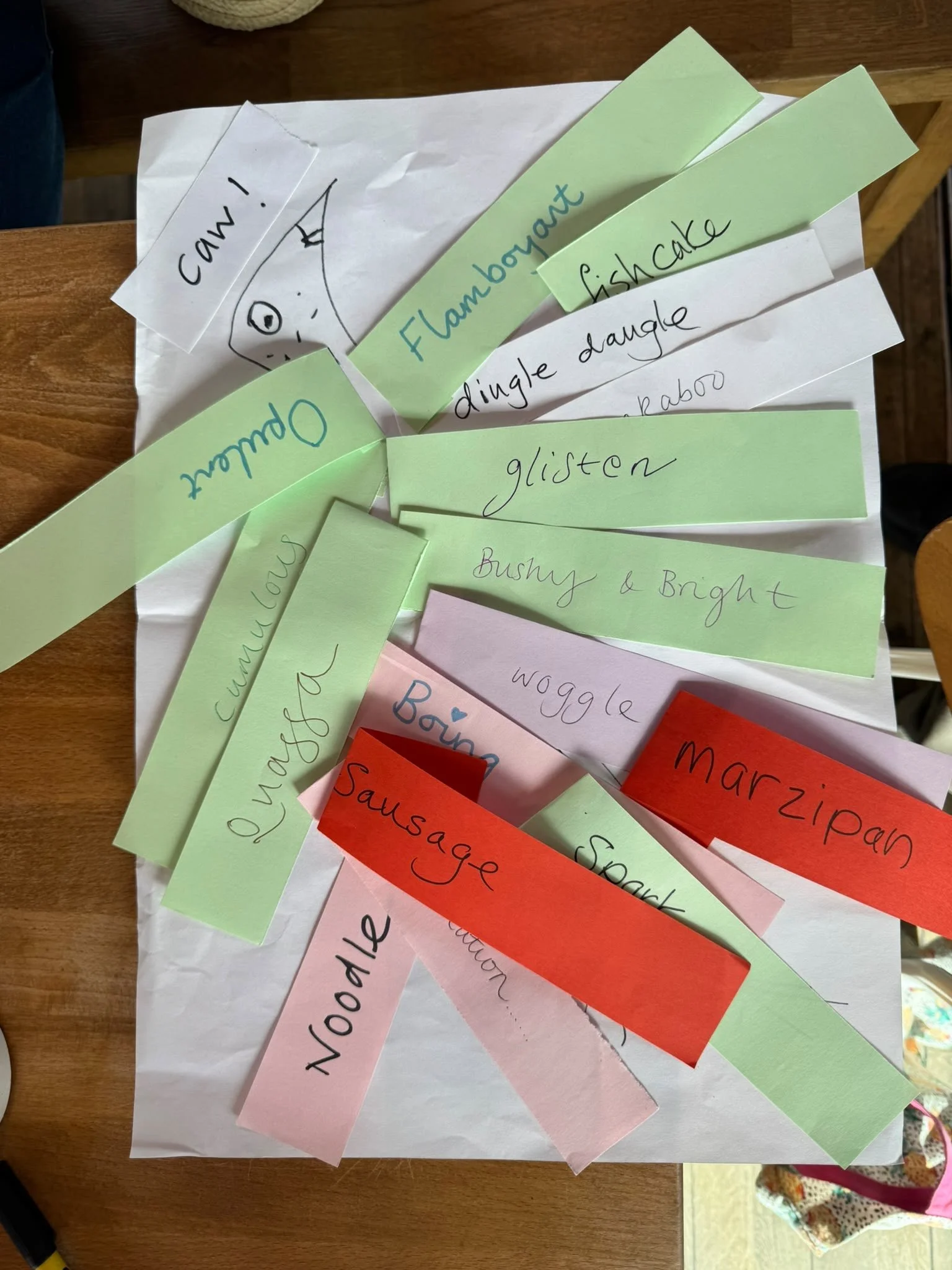Dictionary words are written out on different coloured strips of paper and stuck on a piece of paper to resemble feathers on a bird