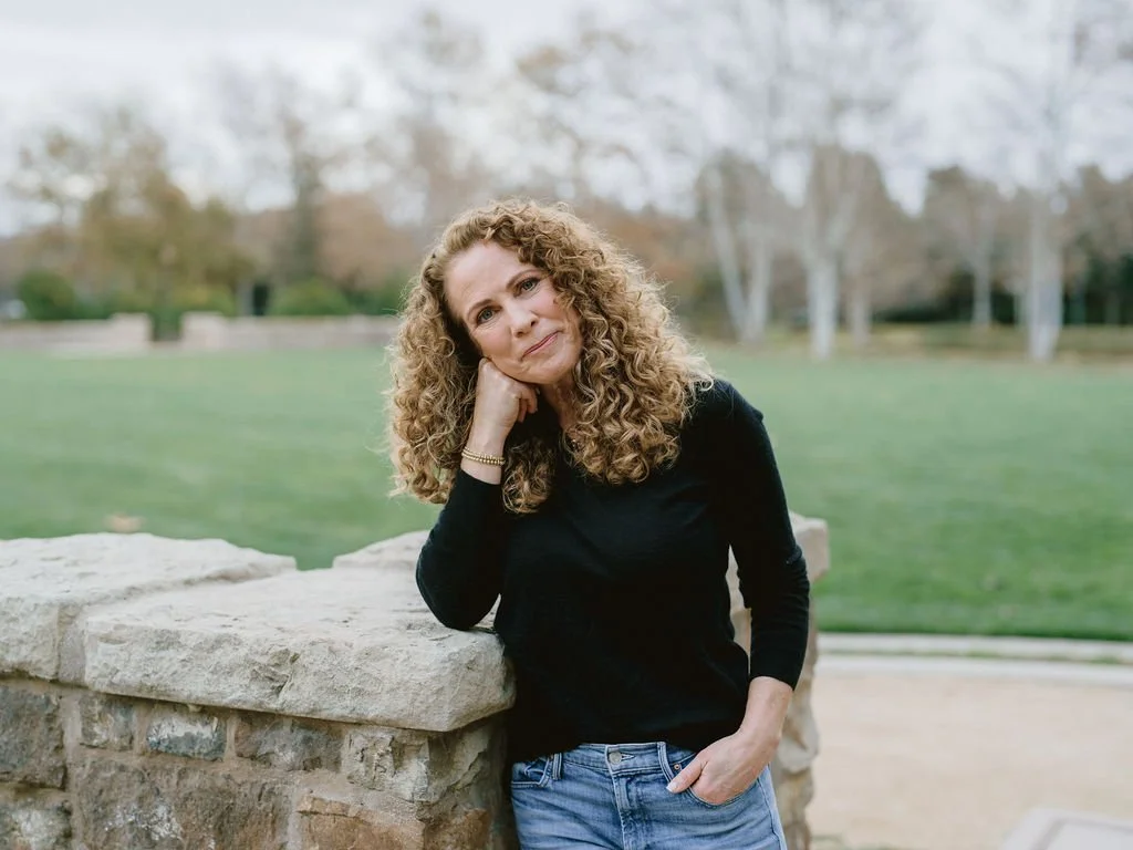 Parenting coach Jeanine Mouchawar standing outdoors, leaning on a stone wall, looking calmly at the camera