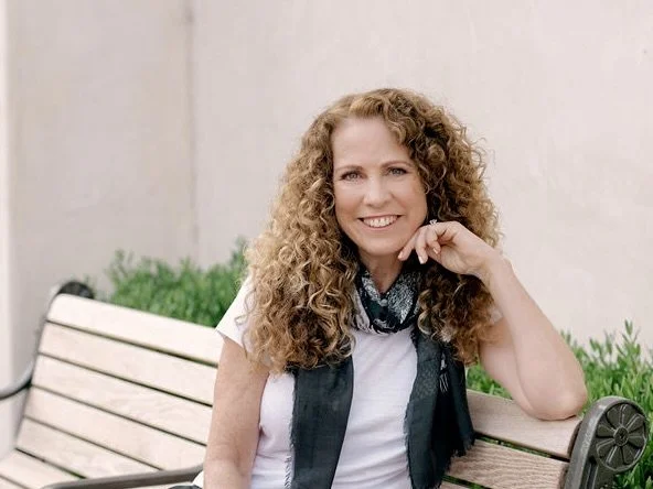 Parenting coach Jeanine Mouchawar smiling while seated on a bench