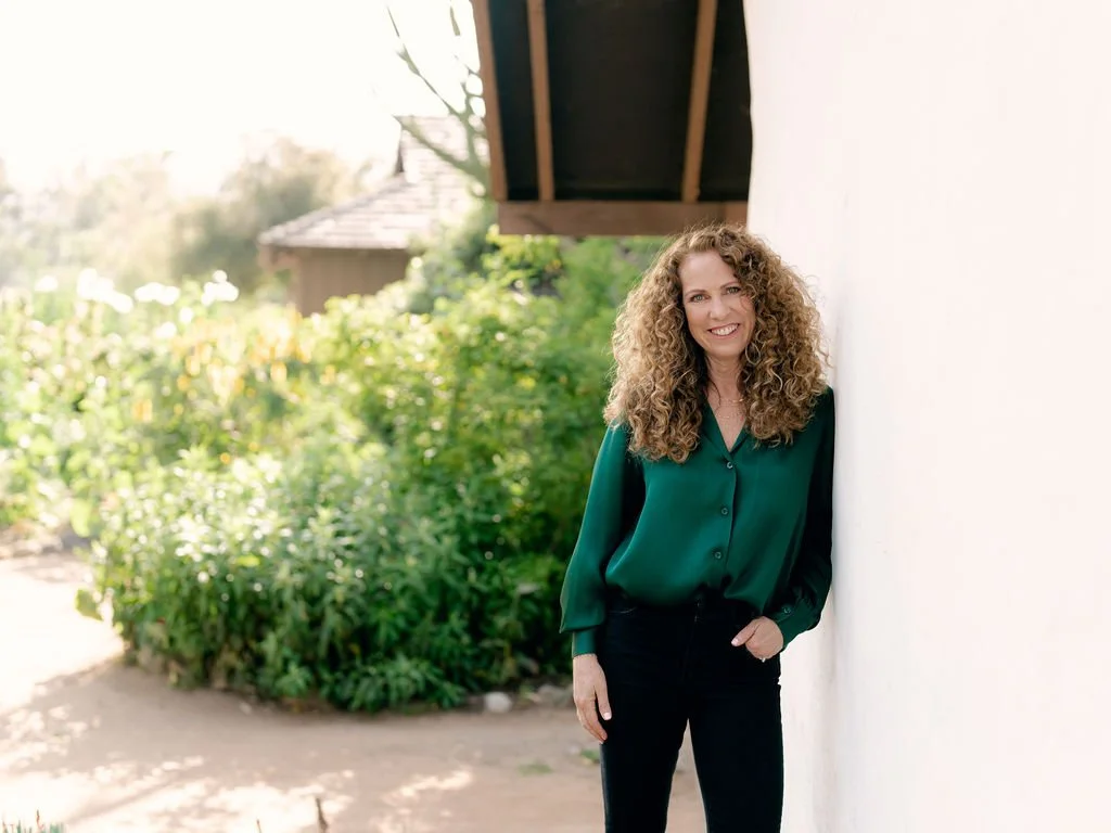 Jeanine Mouchawar smiling outdoors in a green blouse against a white wall