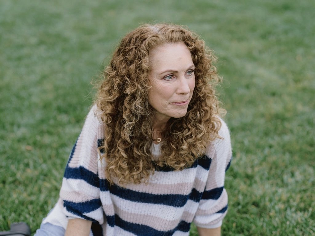 Jeanine Mouchawar, parent coach, sitting on the grass and looking thoughtfully to the side.