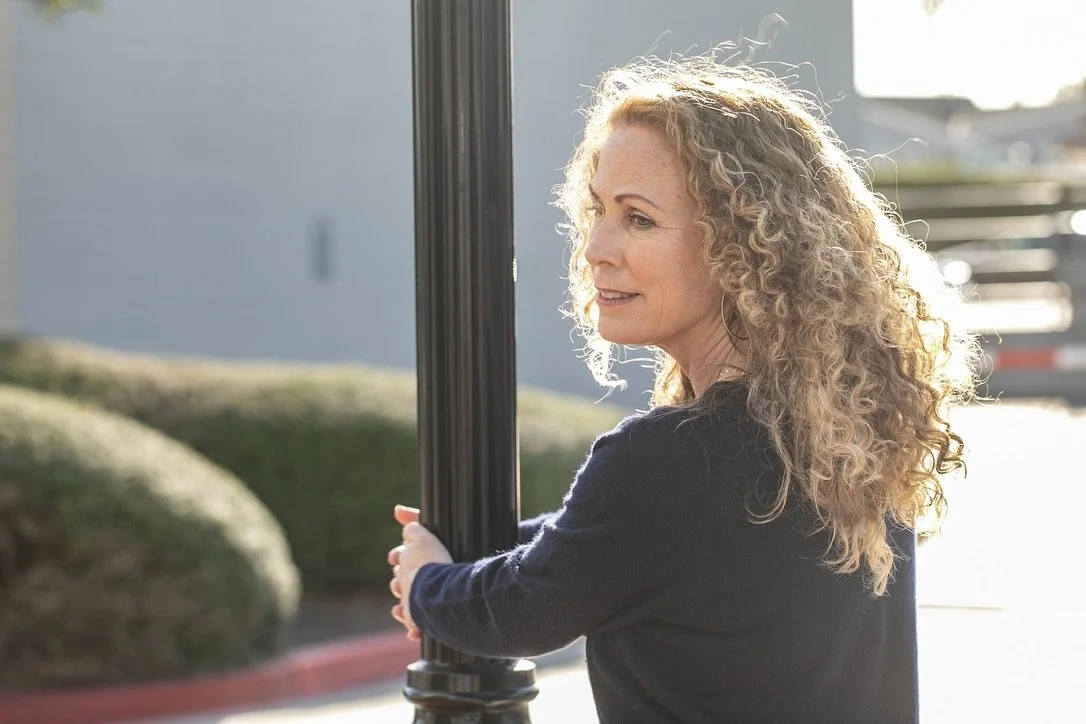 Jeanine Mouchawar, parenting coach, standing outdoors in soft sunlight with a thoughtful expression, reflecting on emotional exhaustion and the hidden weight many parents carry.