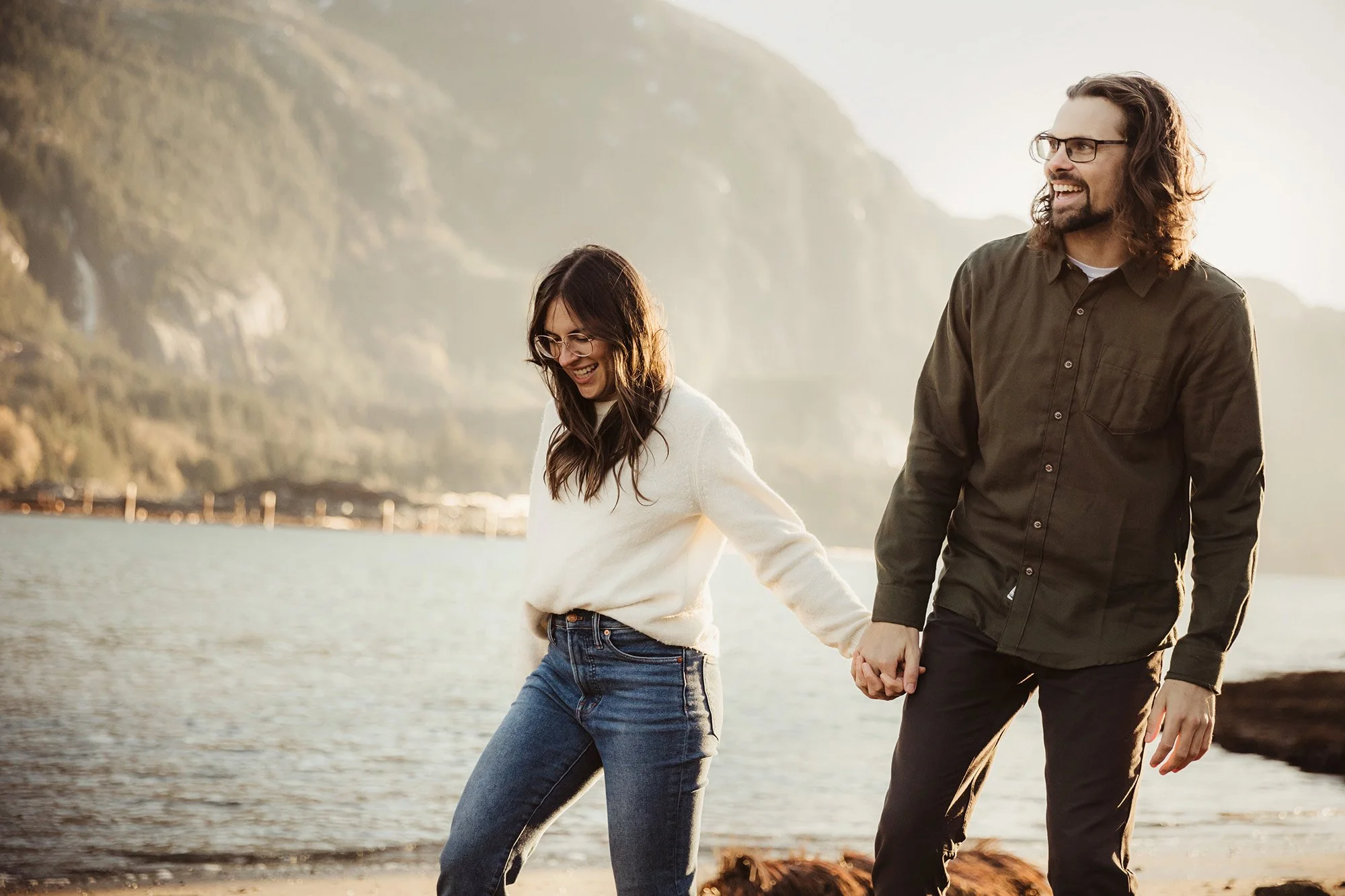 A couple walking hand in hand along a beach with cliffs in the background, smiling and enjoying the moment.